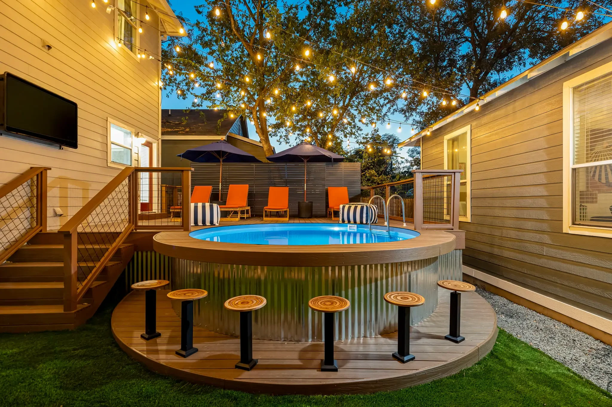 Airbnb backyard design with round pool, corrugated metal pool surround, swim-up bar, and outdoor TV at dusk — Austin TX.
