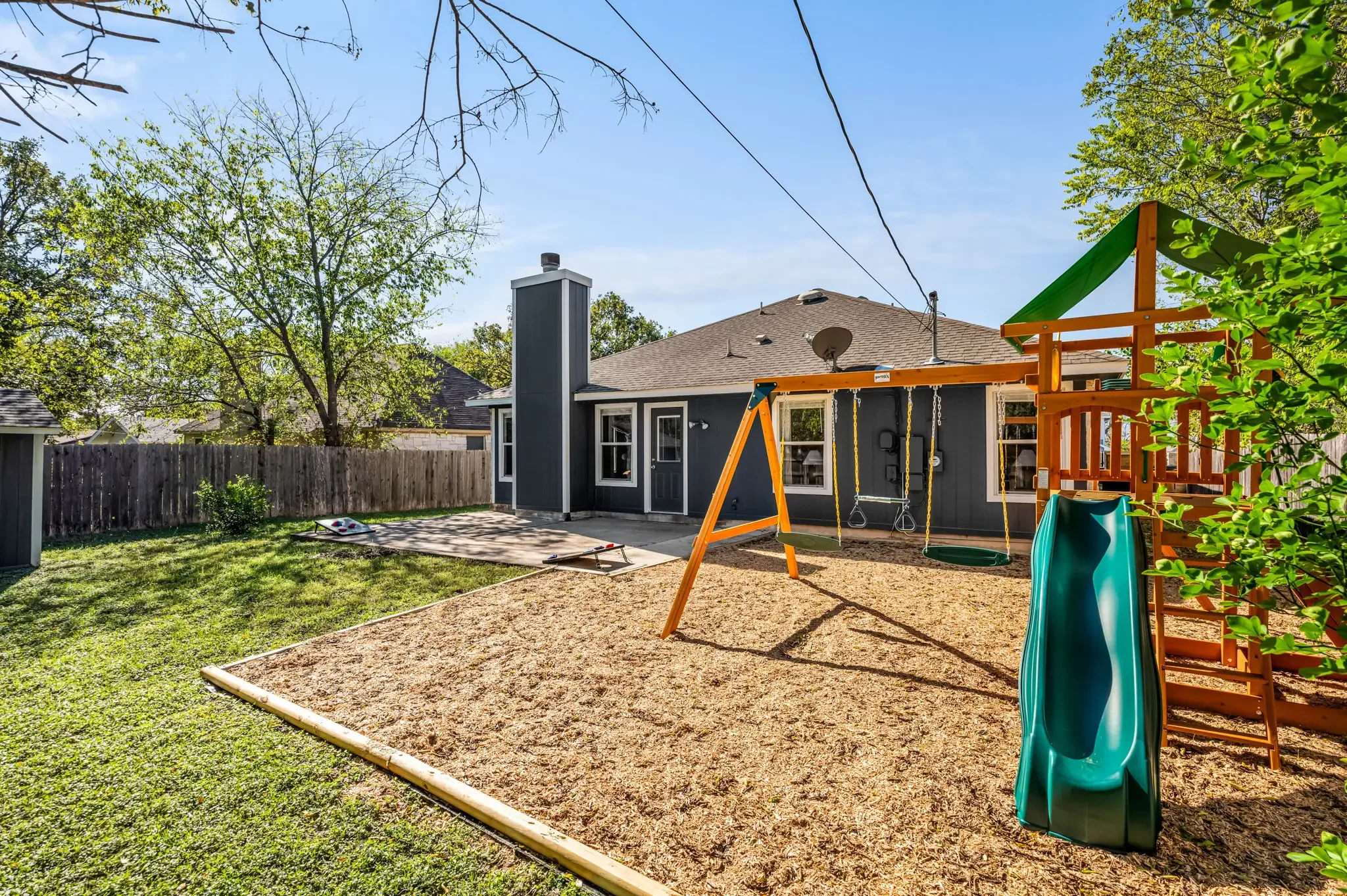 Airbnb backyard design with kids playset, slide, swings, and spacious yard for family short-term rental — Austin TX.