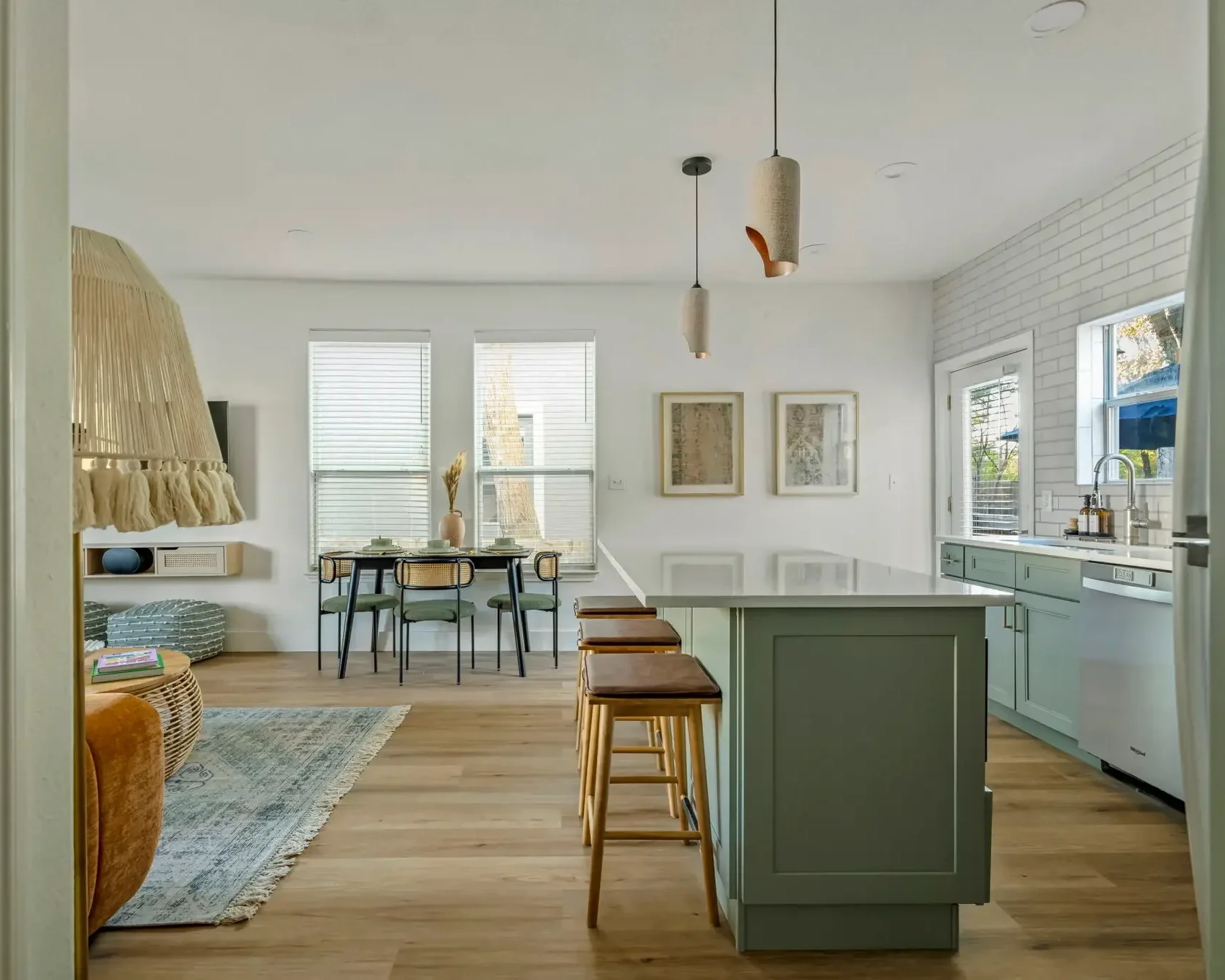 Open-concept vacation rental kitchen and dining area featuring sage green cabinetry, waterfall island, wood flooring, and warm organic finishes.