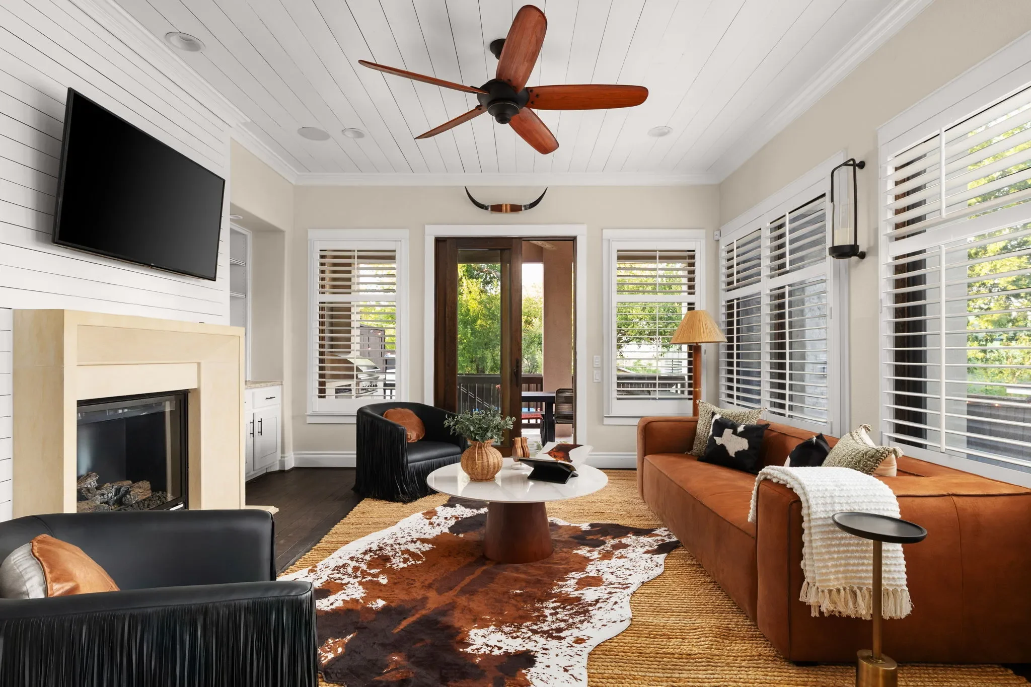 Living room with a brown leather sofa, cowhide rug layered over a jute rug, tasseled accent chairs, and modern western chic decor.