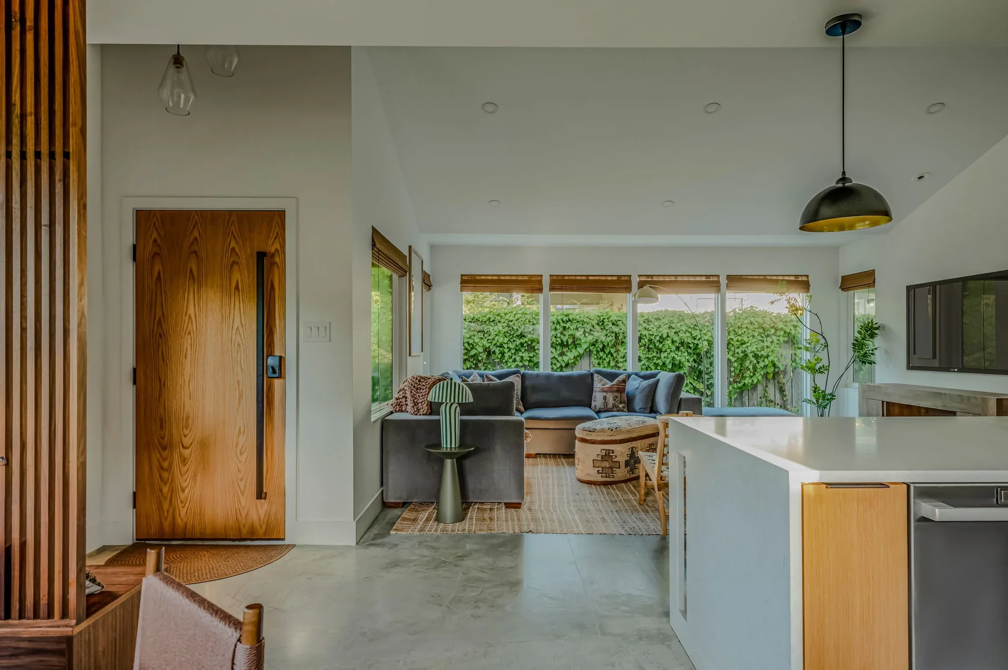 Airbnb entryway design with solid wood door, wood slat partition, and open view to blue sectional living room — Austin TX.