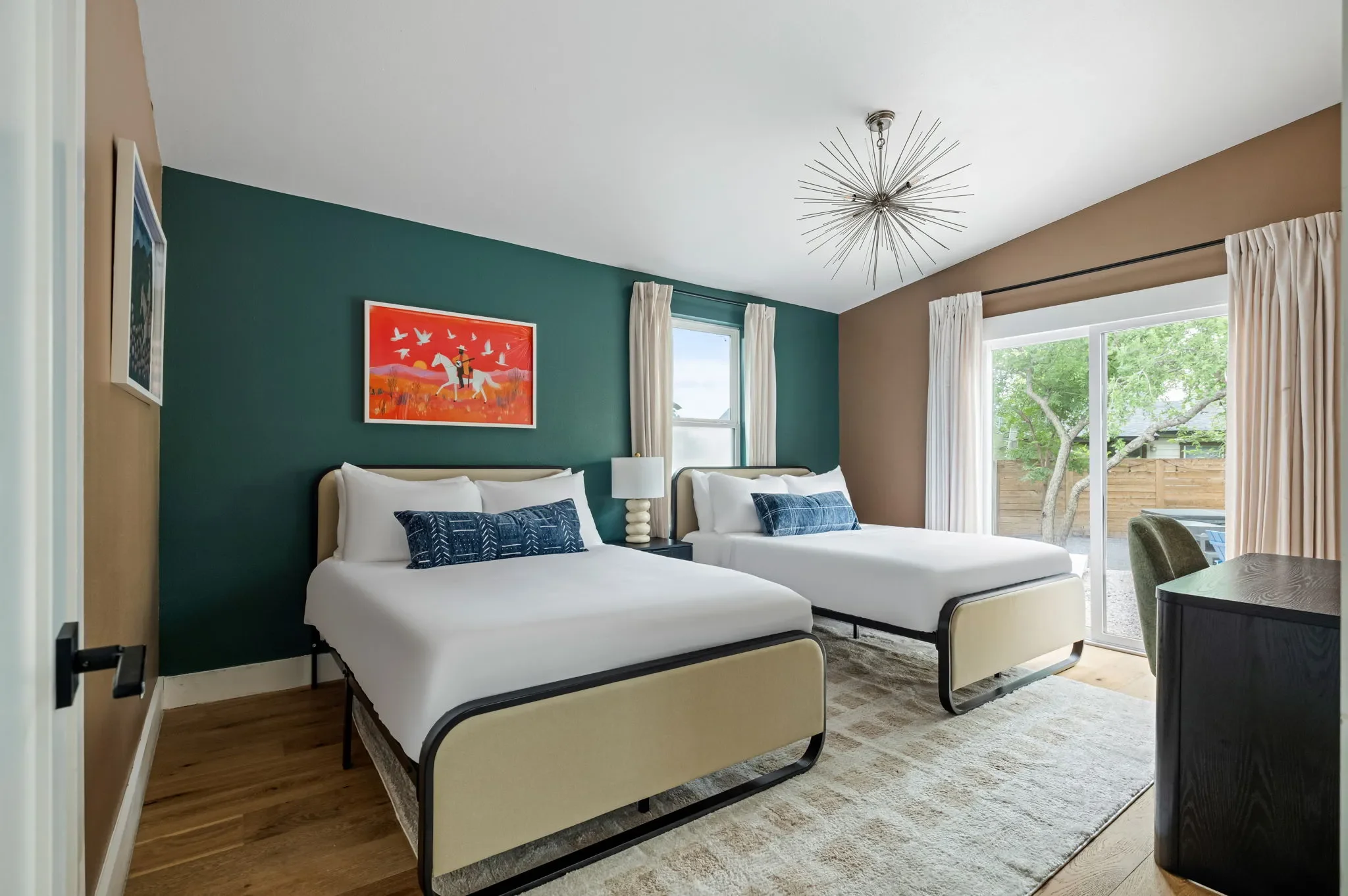 Airbnb double bedroom design with teal accent wall, two queen beds, colorful horse artwork, and sputnik chandelier — Austin TX.