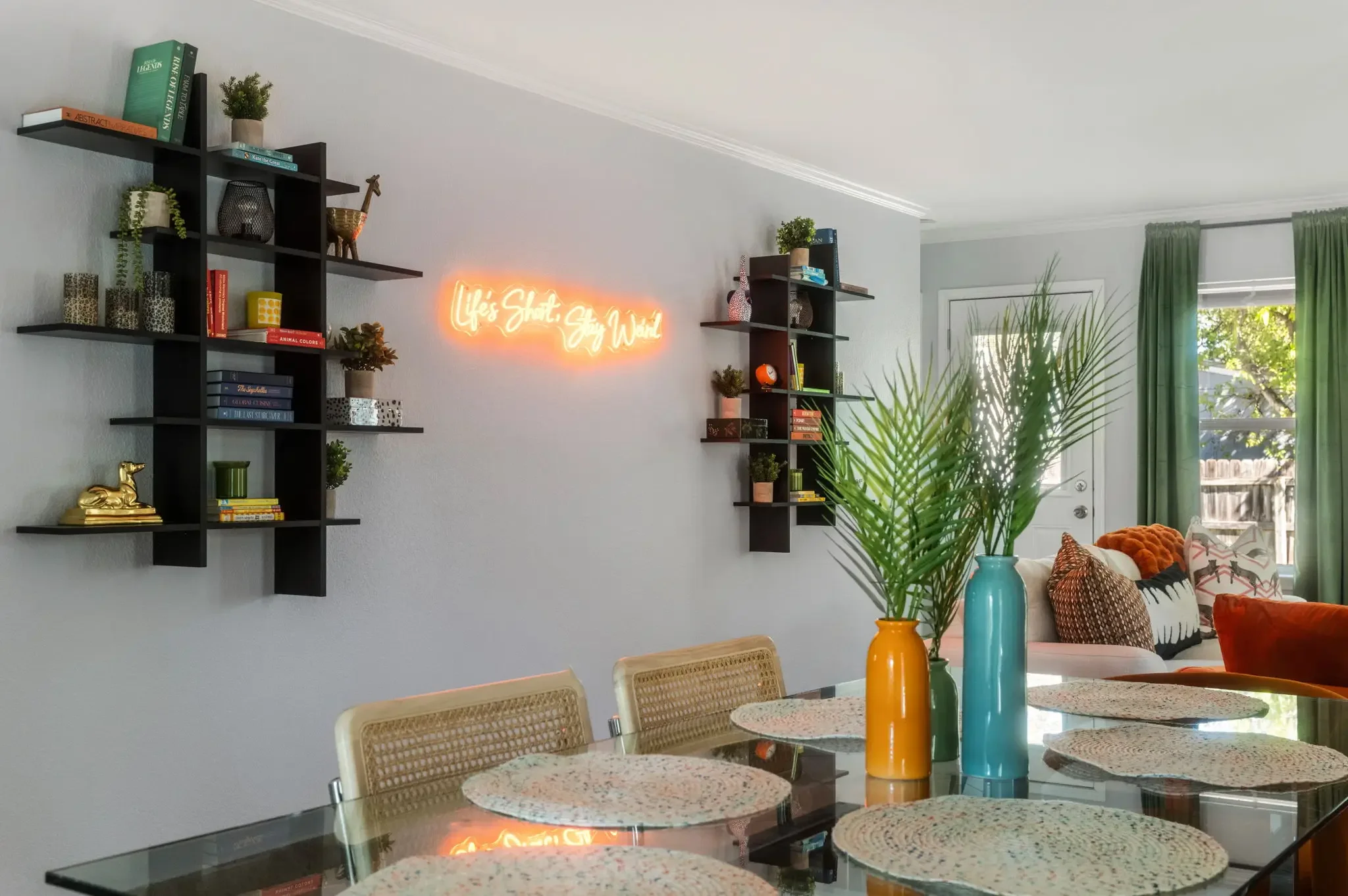 Short-term rental interior design detail with black shelving, neon sign, tropical plants, and colorful decor accents — Austin TX.