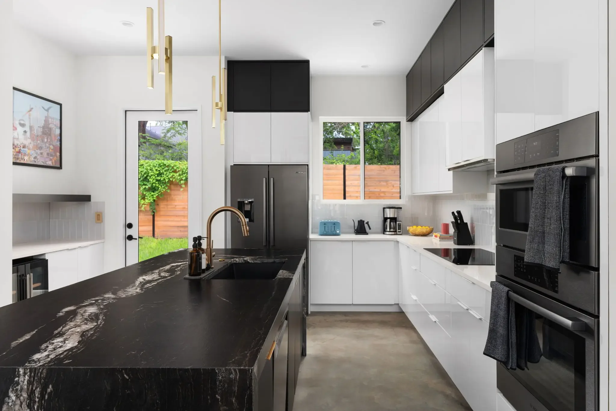 Airbnb kitchen design with black marble waterfall island, black stainless appliances, white lower cabinets, and gold pendant lights — Austin TX.