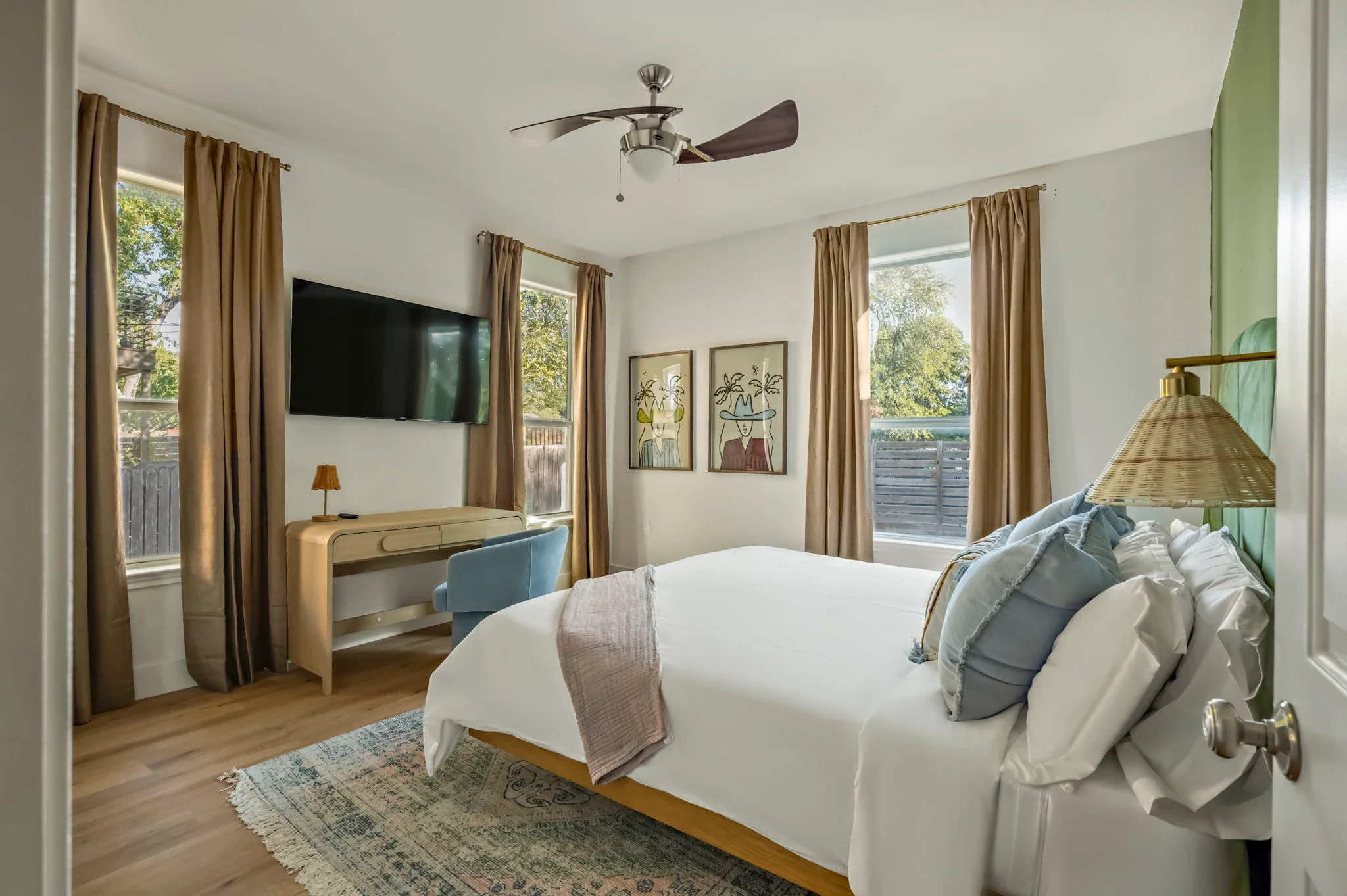 Airbnb bedroom design with TV, wood desk, blue accent chair, layered blue pillows, and printed wall art — Austin TX.