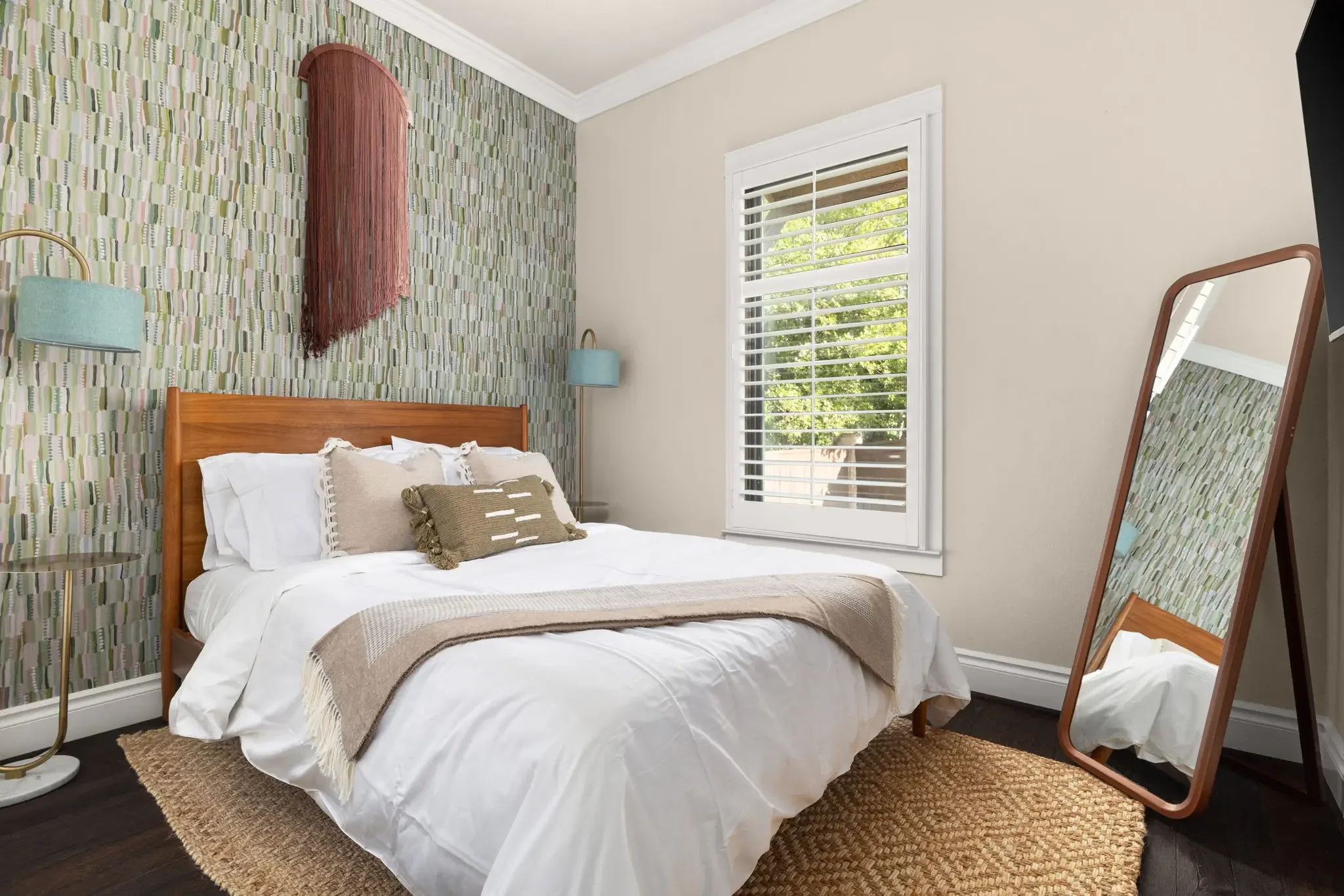 Airbnb bedroom design with green patterned wallpaper, wood headboard, teal sconce, and leaning wood mirror — Austin TX.