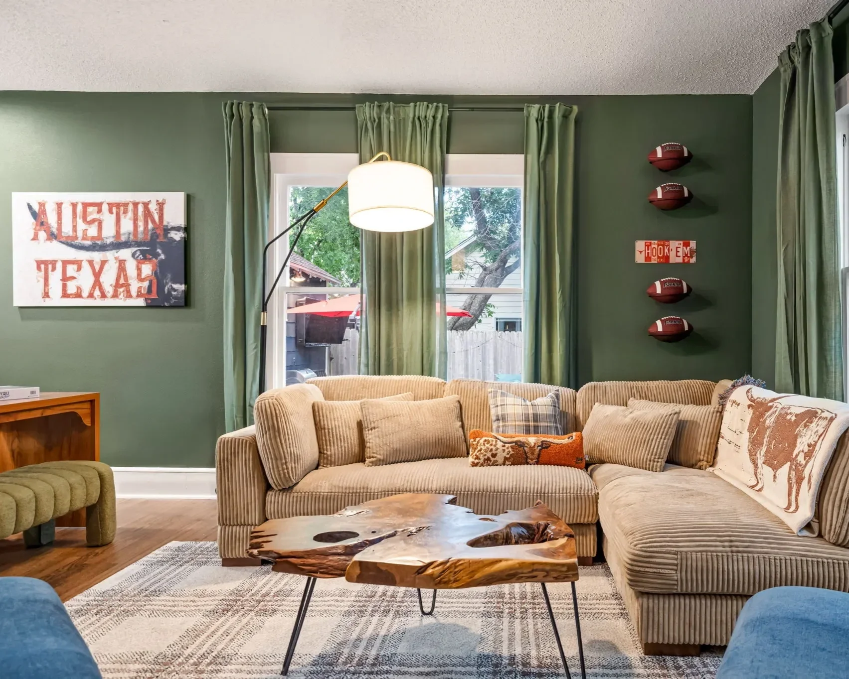 Western Tailgate short-term rental design project — living room with dark green walls, neutral sectional, live edge coffee table, and Austin Texas wall art.