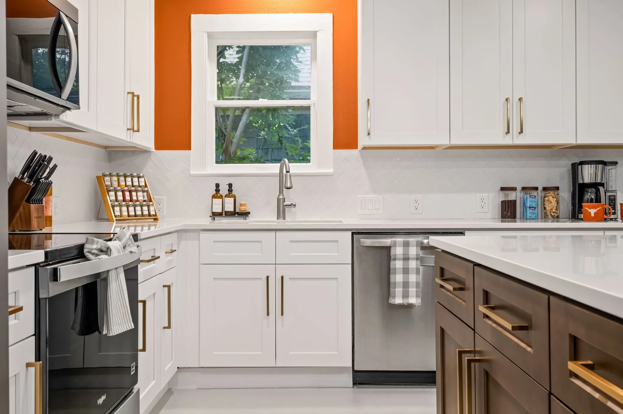 Airbnb kitchen design detail with white cabinets, orange accent wall, gold hardware, stainless appliances, and fully stocked countertops — Austin TX.