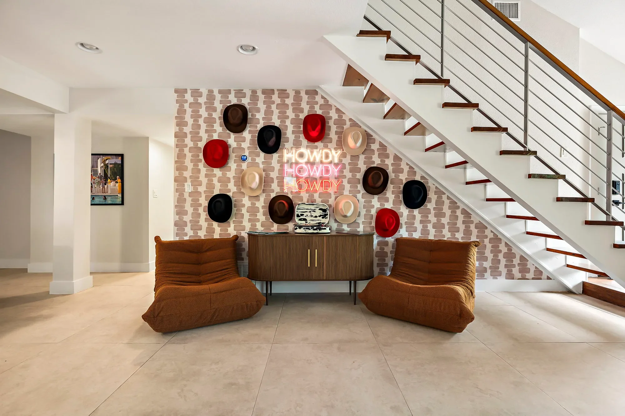 Short-term rental lounge featuring cowboy hat feature wall, “Howdy” neon sign, rust-colored lounge chairs, and a record player.