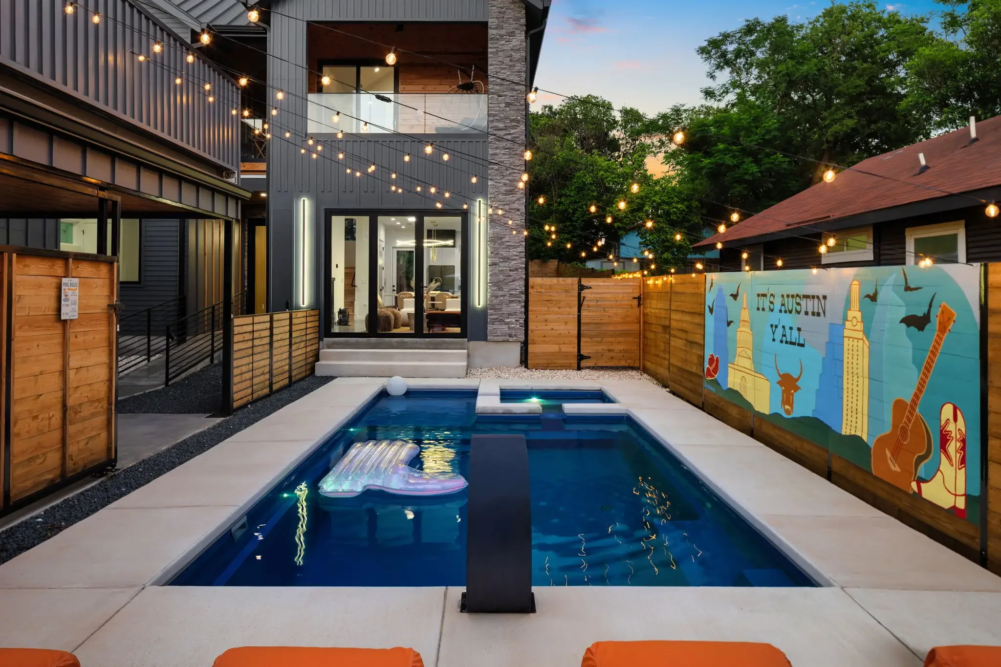 Short-term rental backyard design with plunge pool, Austin skyline mural, string lights, and modern home exterior at dusk — Austin TX.