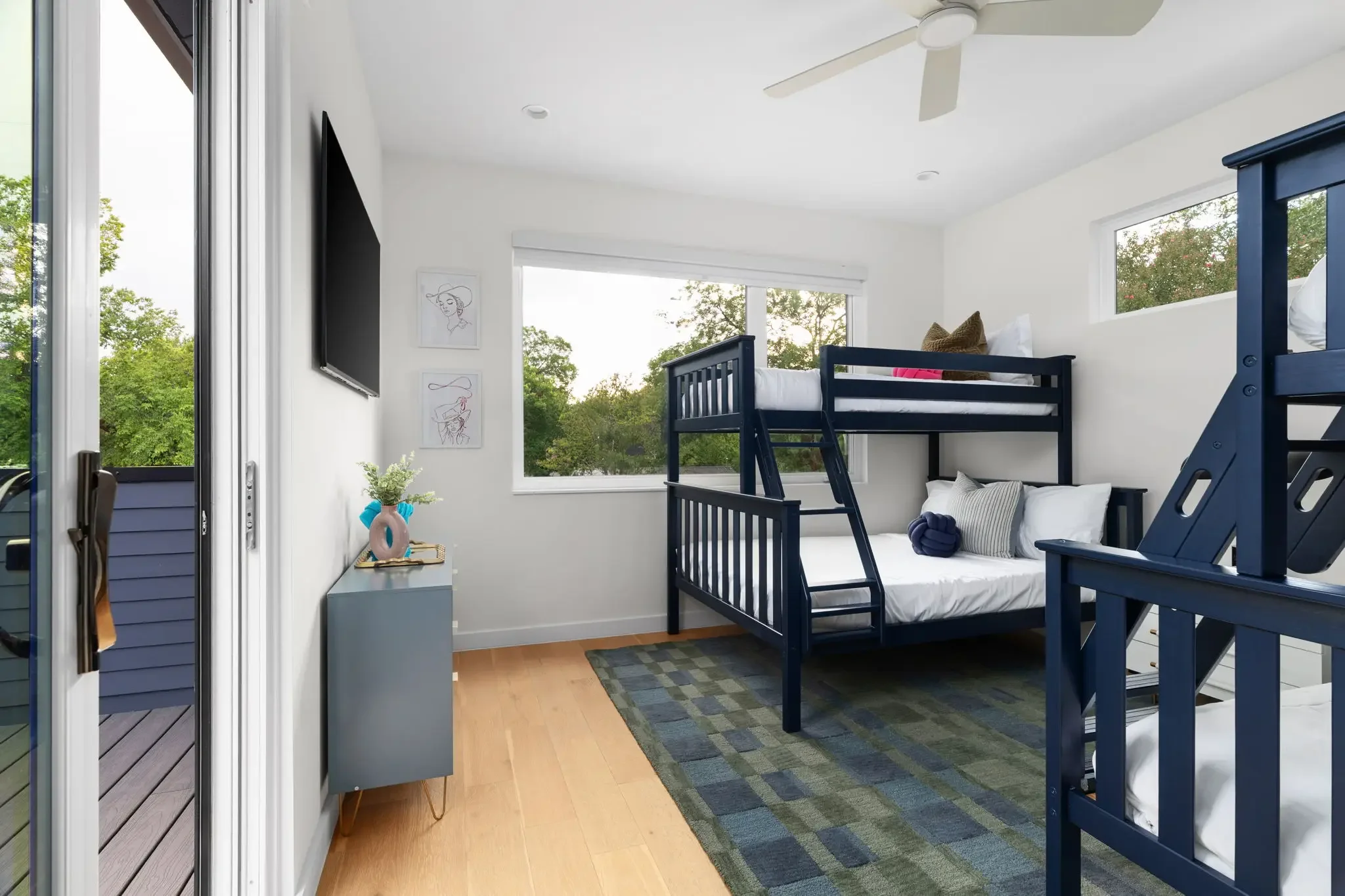 Airbnb bunk room design with navy twin-over-full bunk beds, sliding glass door to deck, TV, and playful line art — Austin TX.