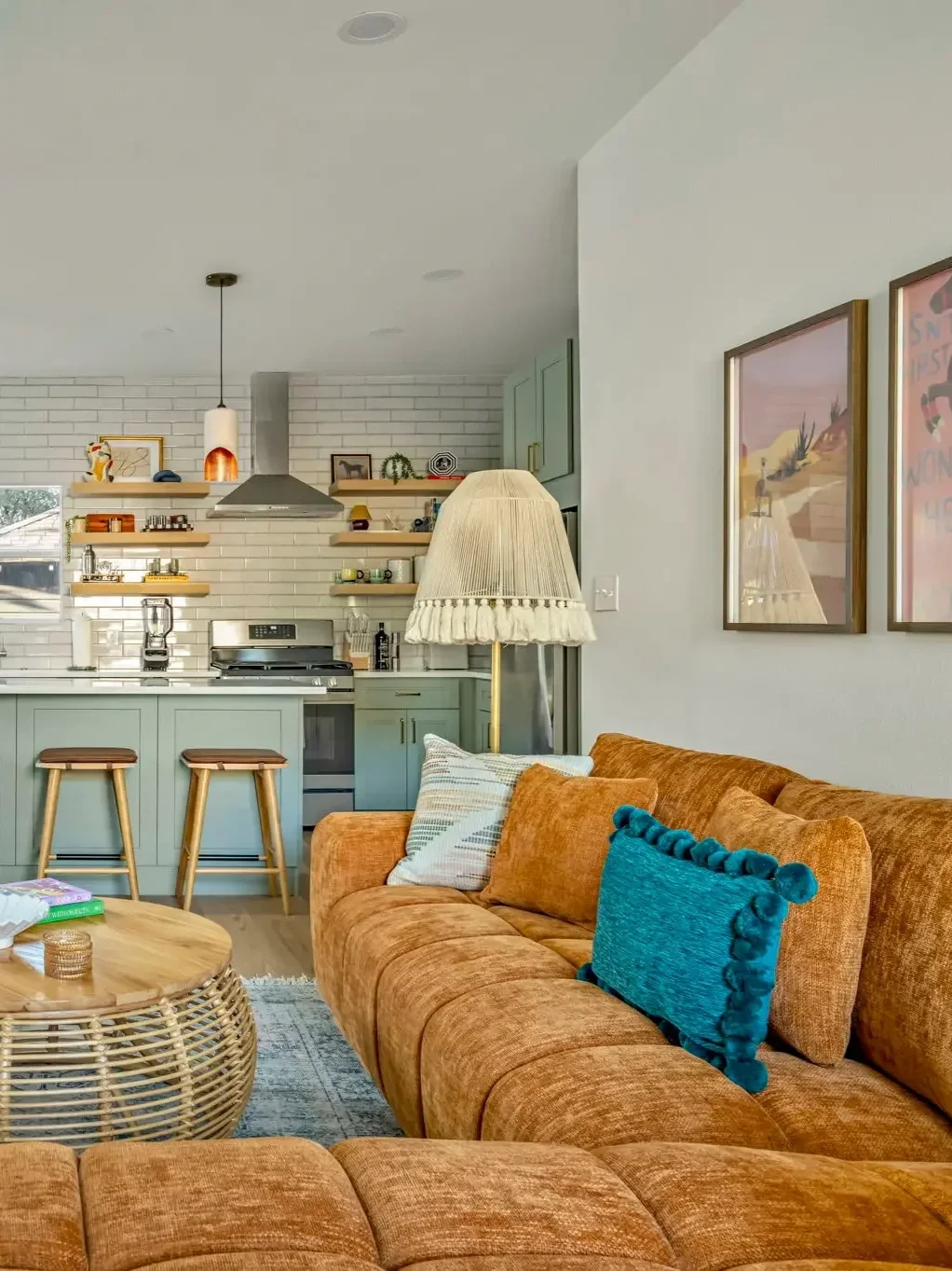 Short-term rental interior design with sage green kitchen, tan sectional, teal pillows, and colorful wall art — House of Ellie Interiors Austin TX.