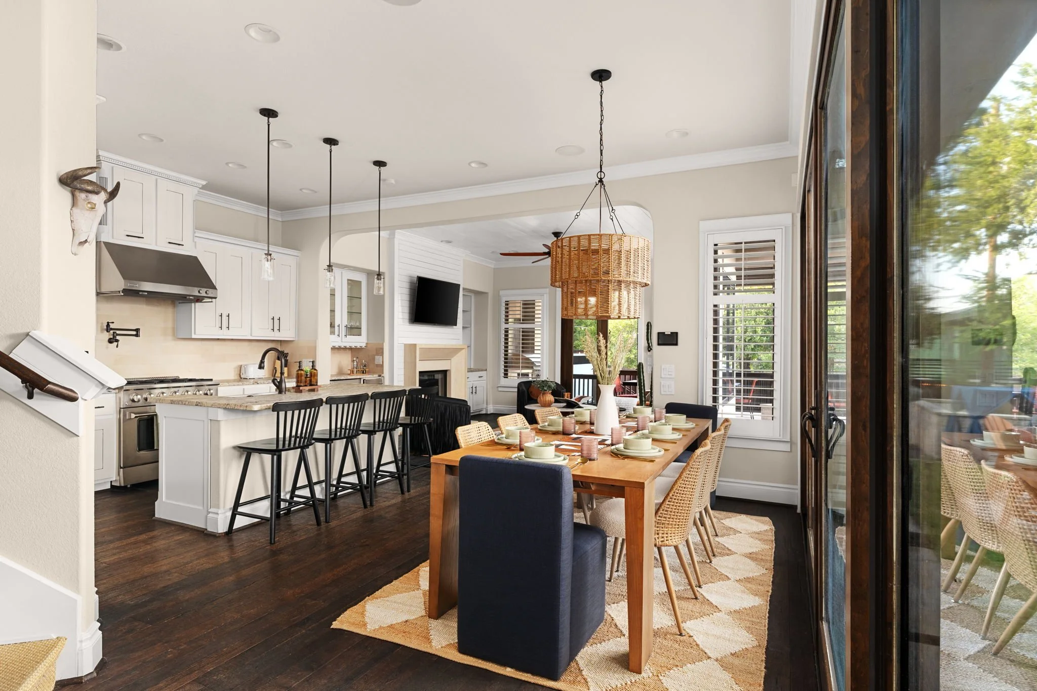 Western-inspired dining space featuring a rattan pendant, long wooden table, cowboy hat accent wall, and kitchen island with black barstools.