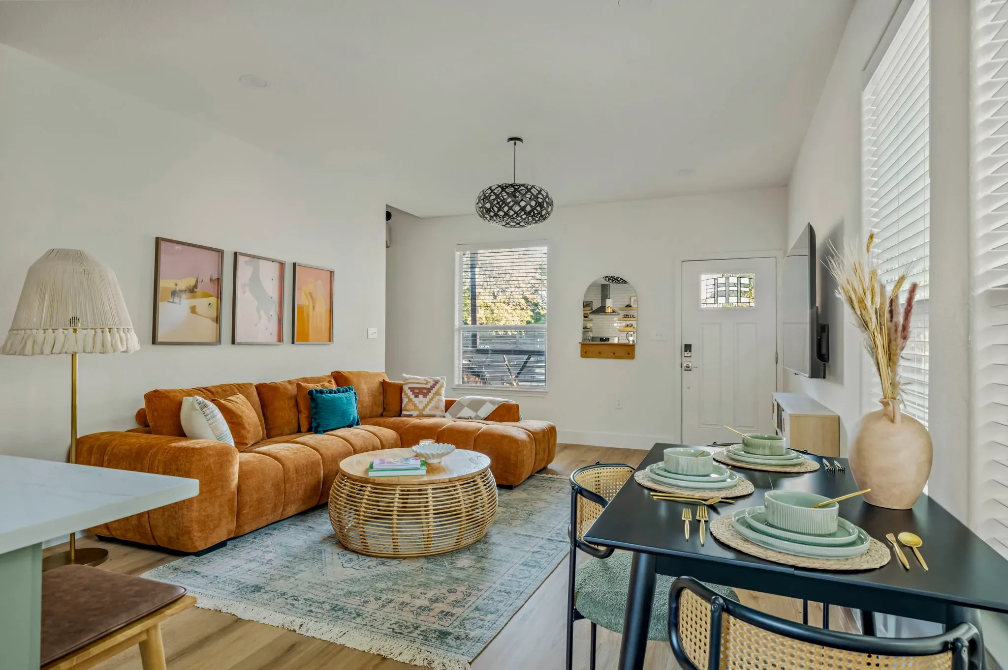Short-term rental living and dining room design with rust velvet sectional, rattan coffee table, fringe lamp, and black dining table — Austin TX.