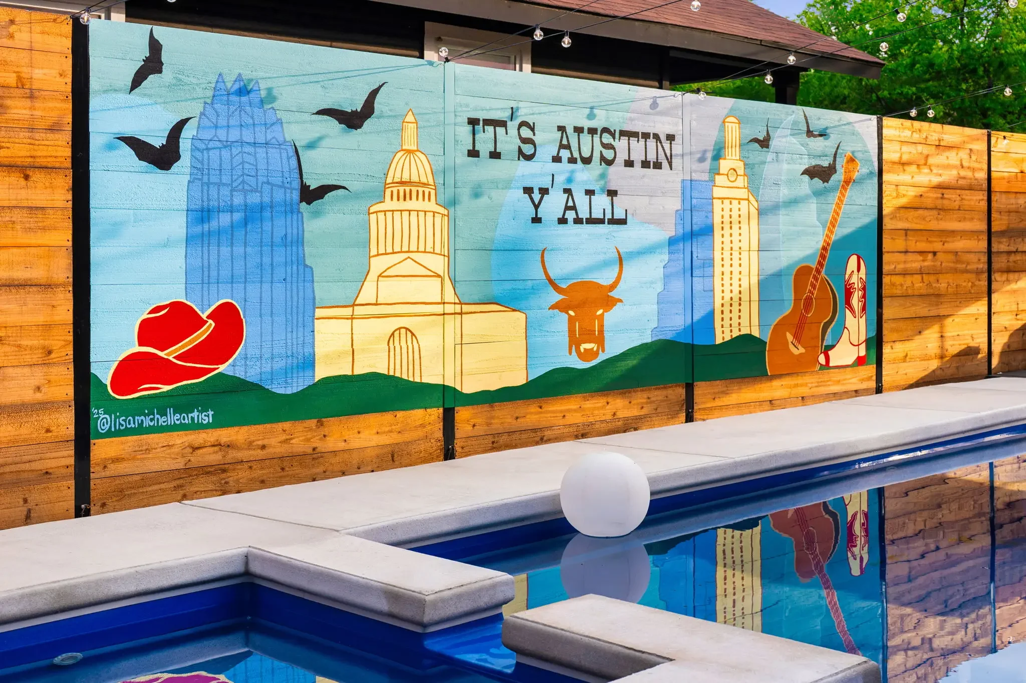 Short-term rental pool design detail with custom Austin Y'all skyline mural on wood fence and floating pool light — Austin TX.