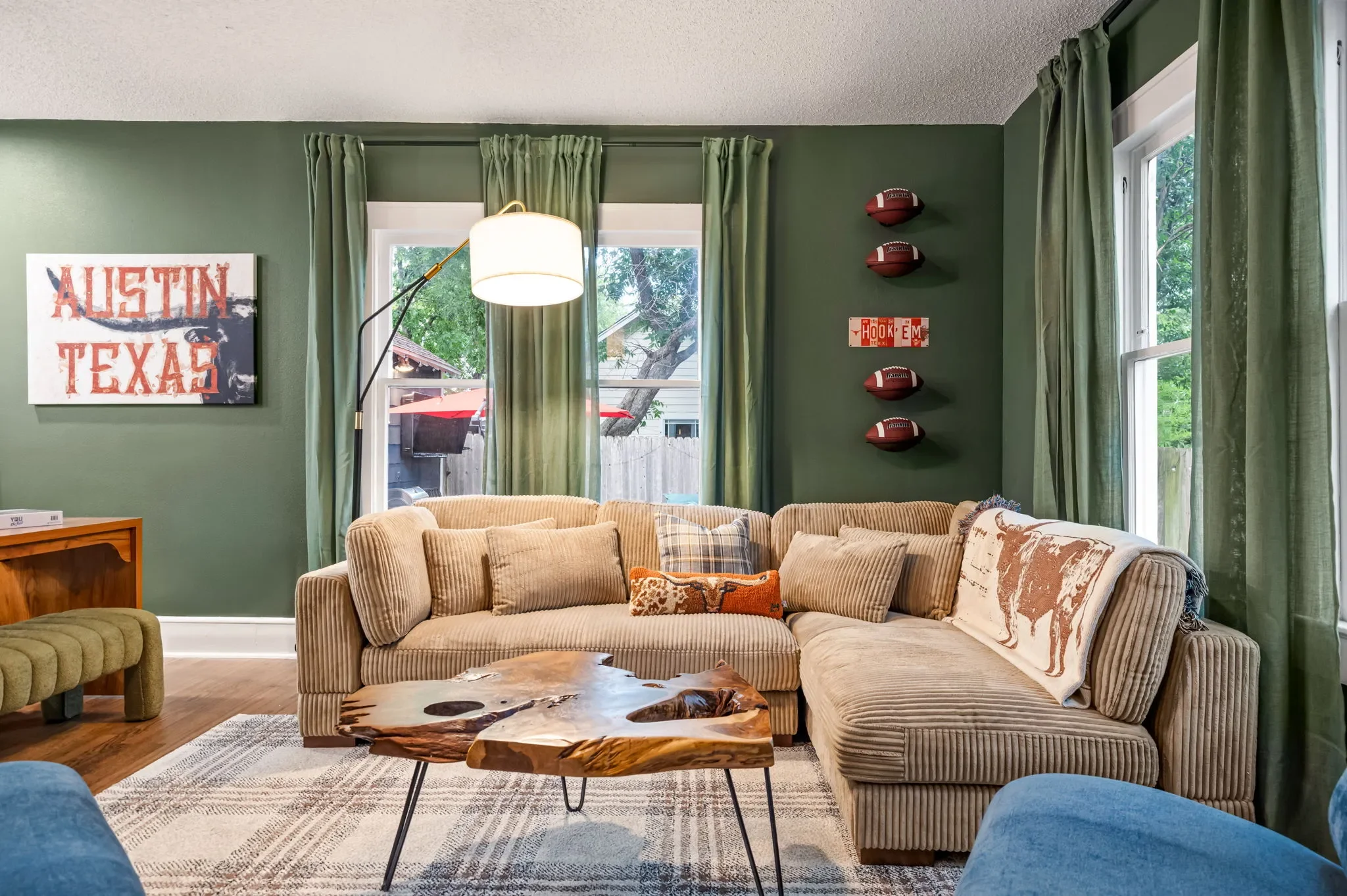 Short-term rental living room design with dark green walls, tan corduroy sectional, live edge coffee table, football wall decor, and Austin Texas art — Austin TX.