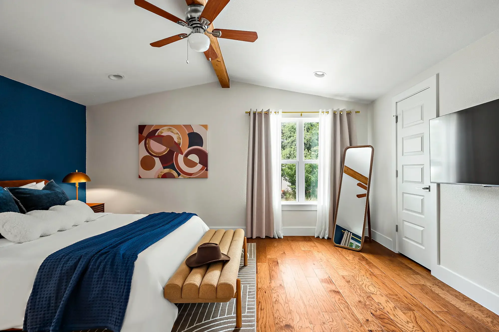 Airbnb bedroom design with navy accent wall, orange velvet headboard, leaning mirror, TV, and abstract wall art — Austin TX.