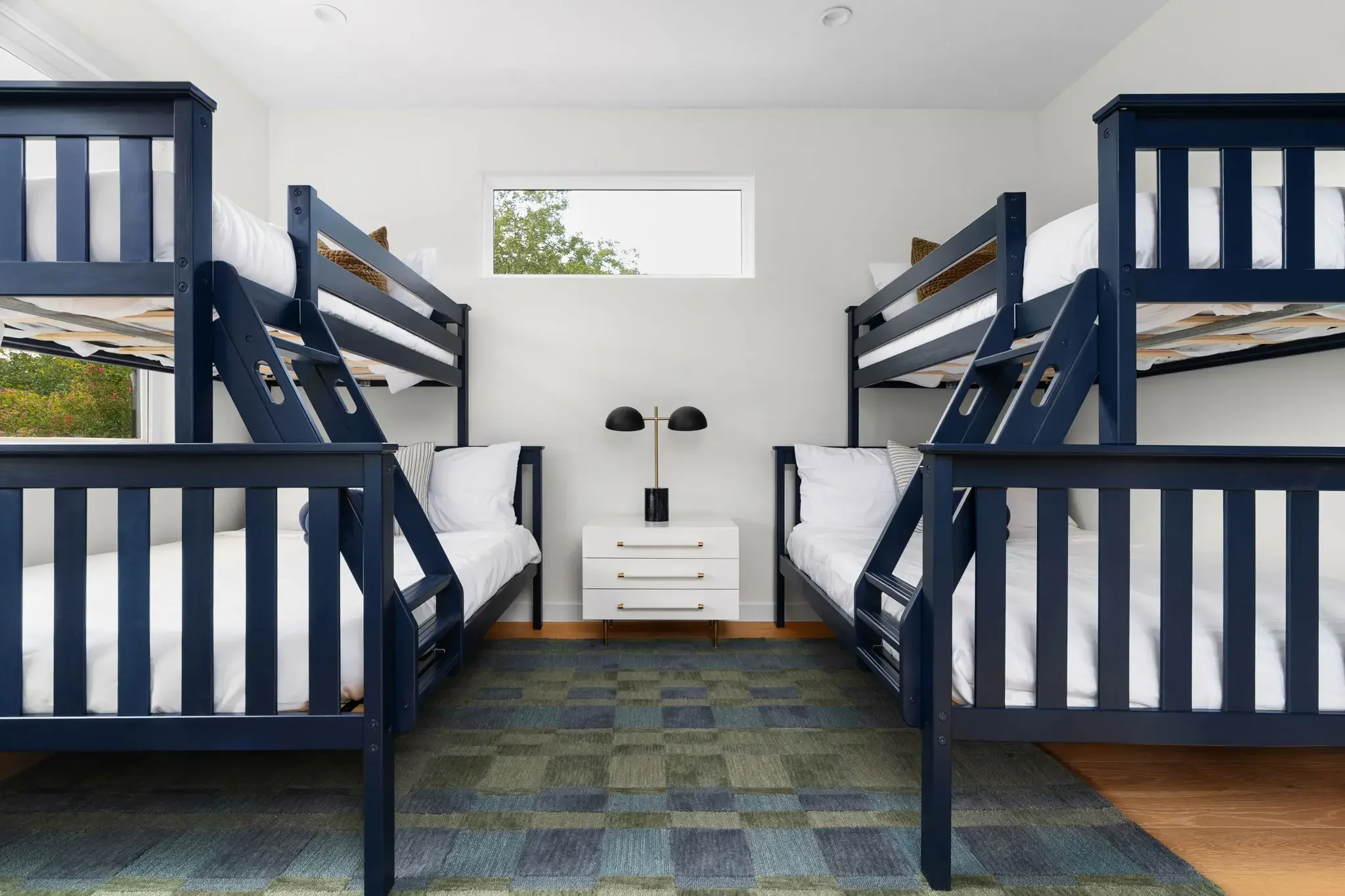 Short-term rental bunk room design with navy twin-over-full bunk beds, white nightstand, and blue and green checkered rug — Austin TX.