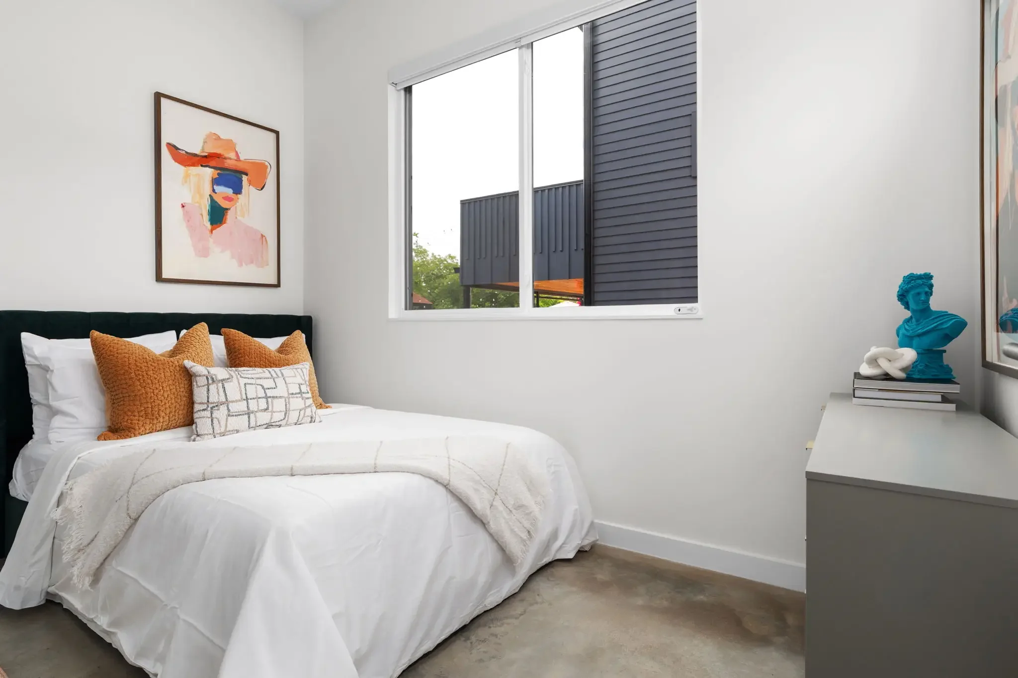 Airbnb bedroom design with black velvet tufted headboard, rust orange pillows, blue bust statue, and colorful portrait art — Austin TX.