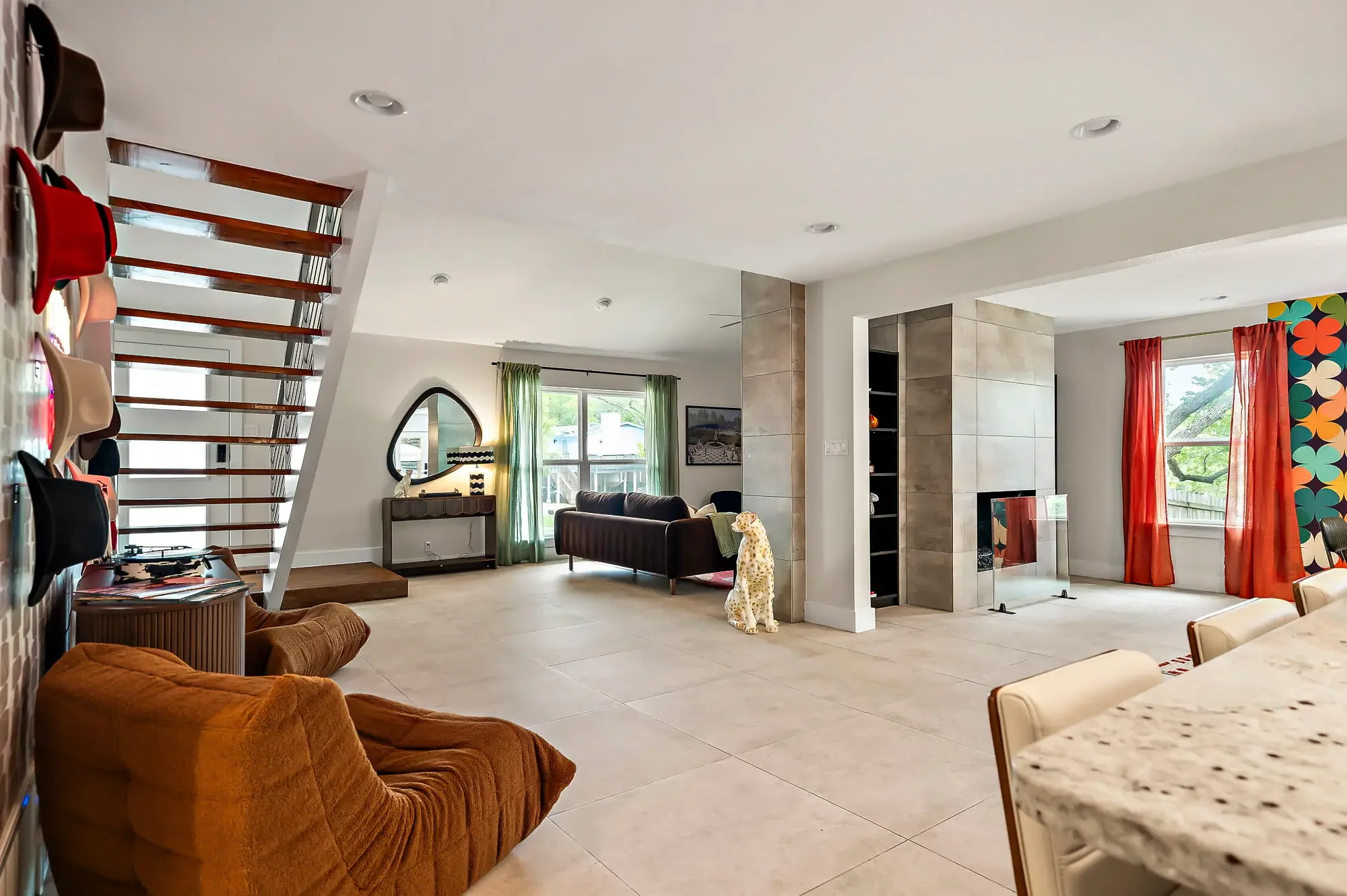 Short-term rental ground floor design with open layout, togo chairs, floating staircase, dalmatian statue, and red and orange curtains — Austin TX.