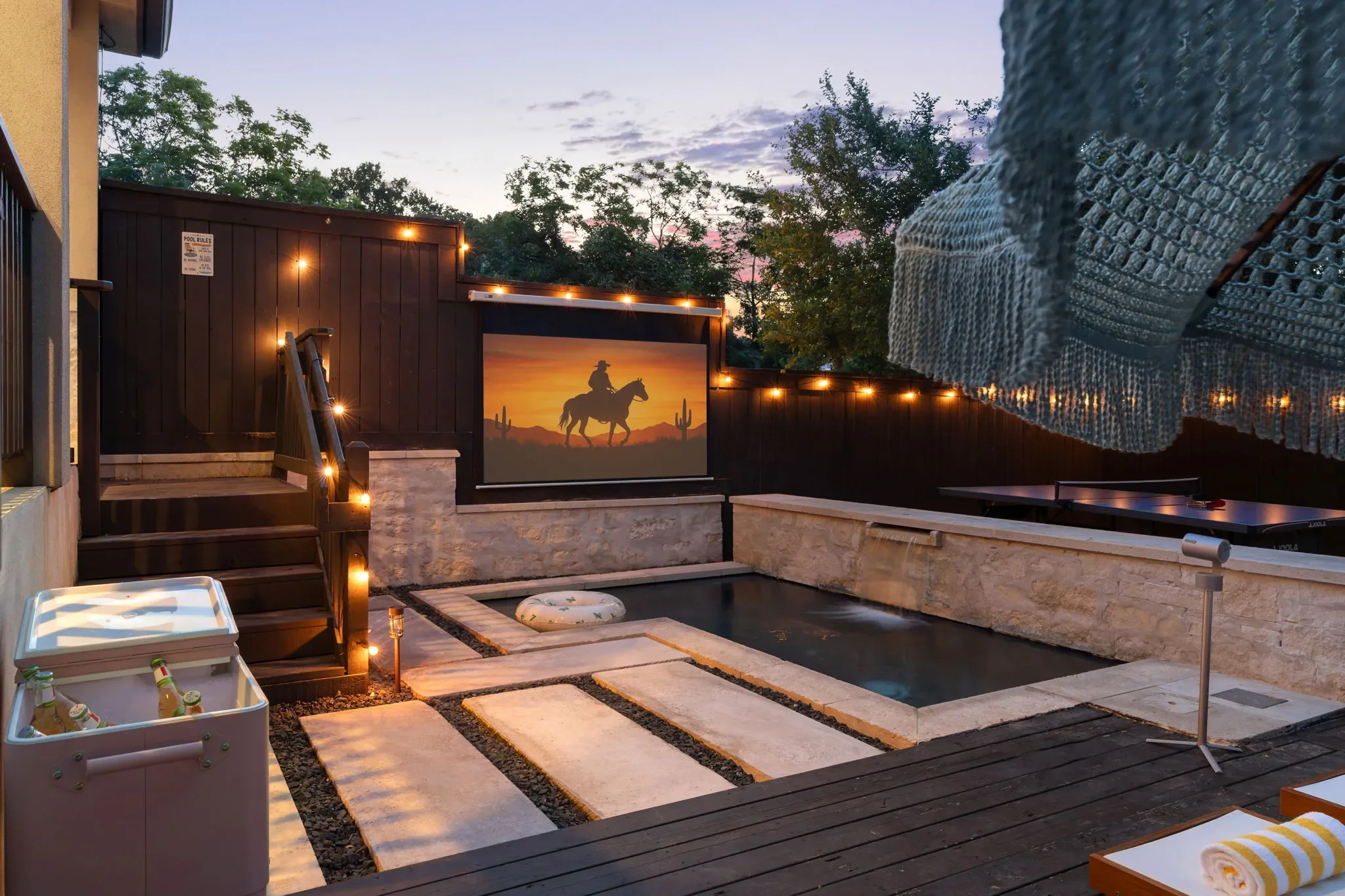 Short-term rental outdoor design with plunge pool, string lights, and outdoor movie screen at dusk — Austin TX.