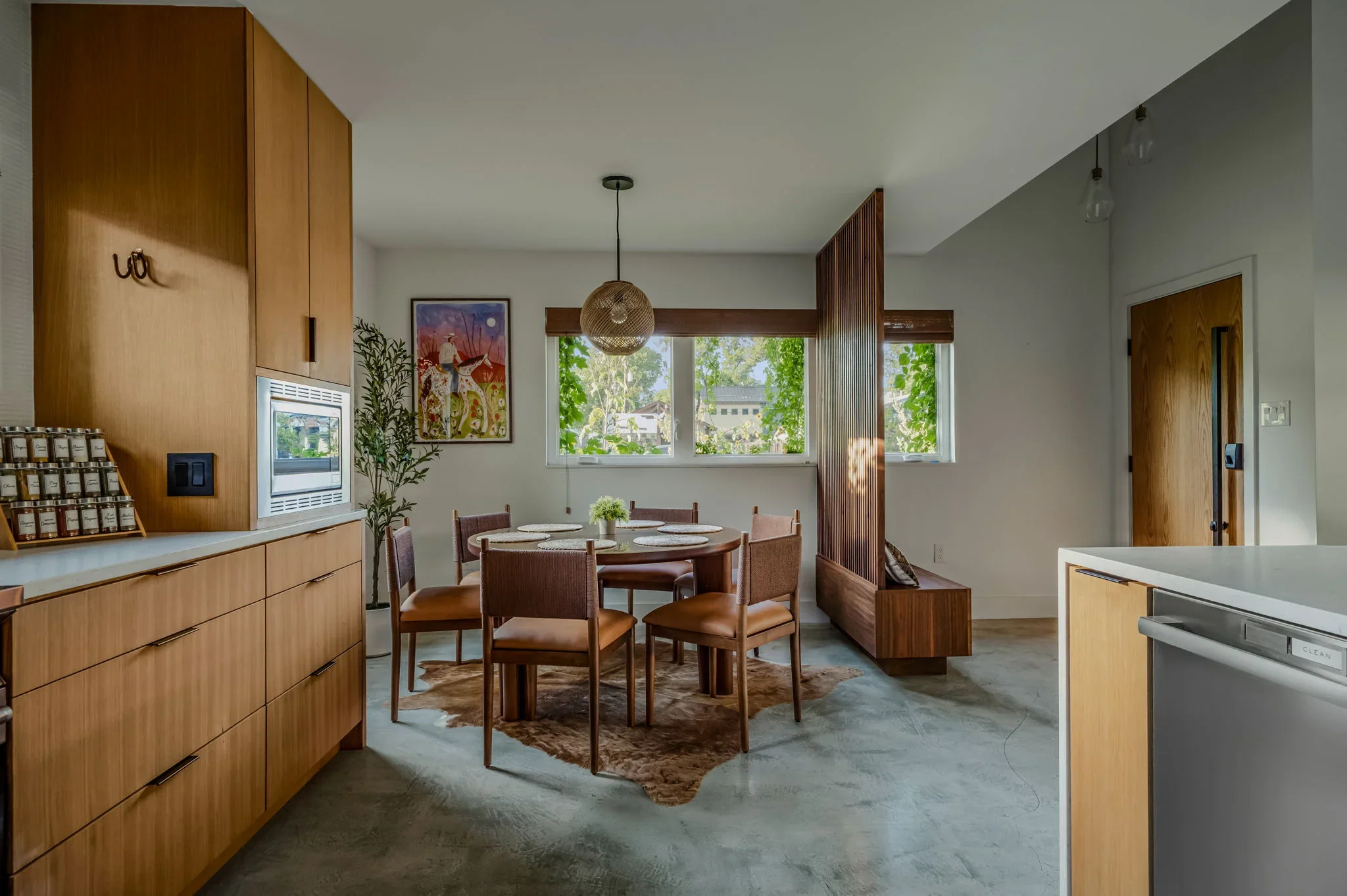 Airbnb dining nook design with wood banquette, round dining table, warm wood cabinetry, and wildflower art — Austin TX.