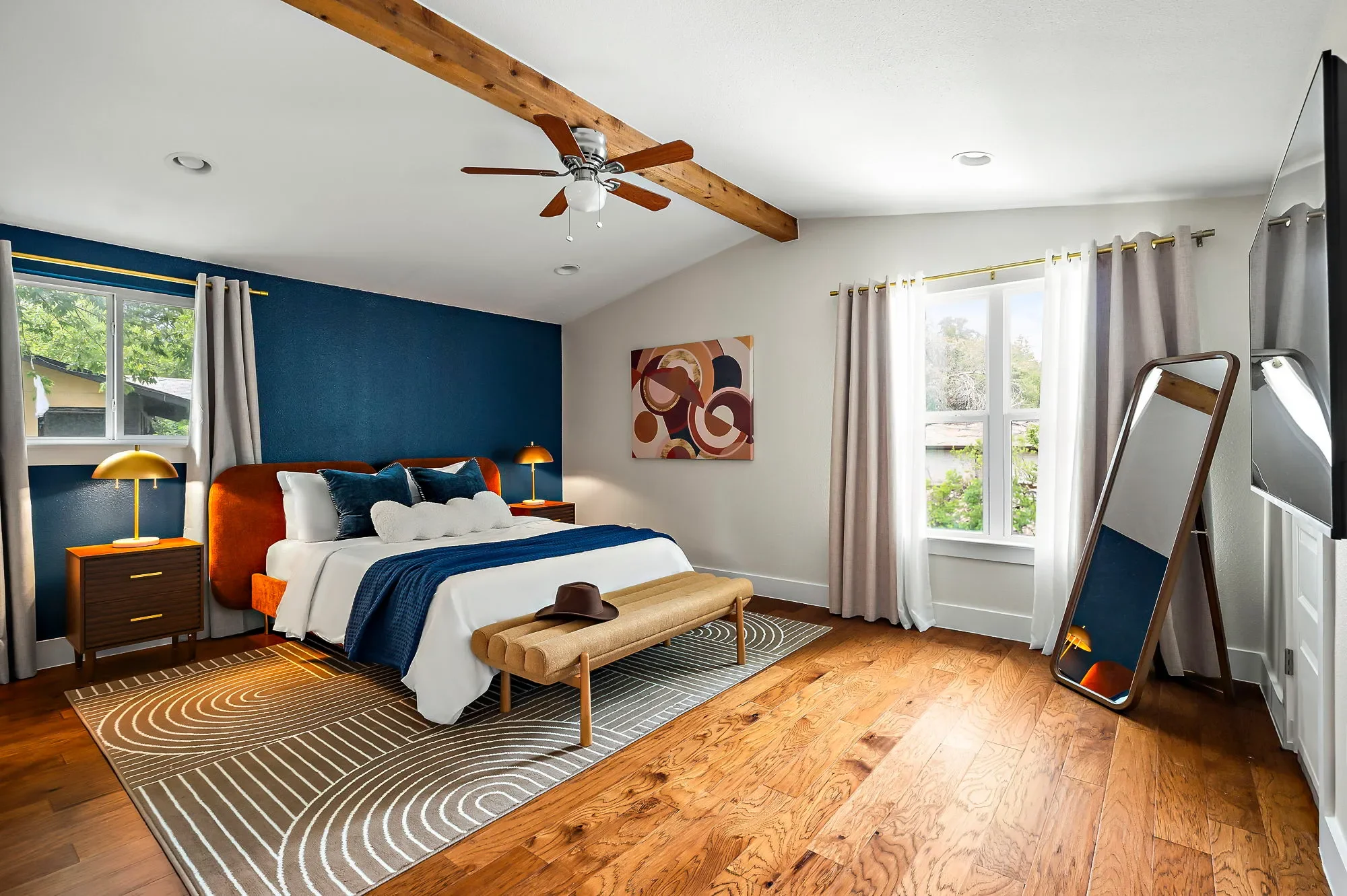 Mid-century modern bedroom featuring navy walls, bright orange bed frame, geometric wall art, beige curtains, and full-length mirror.