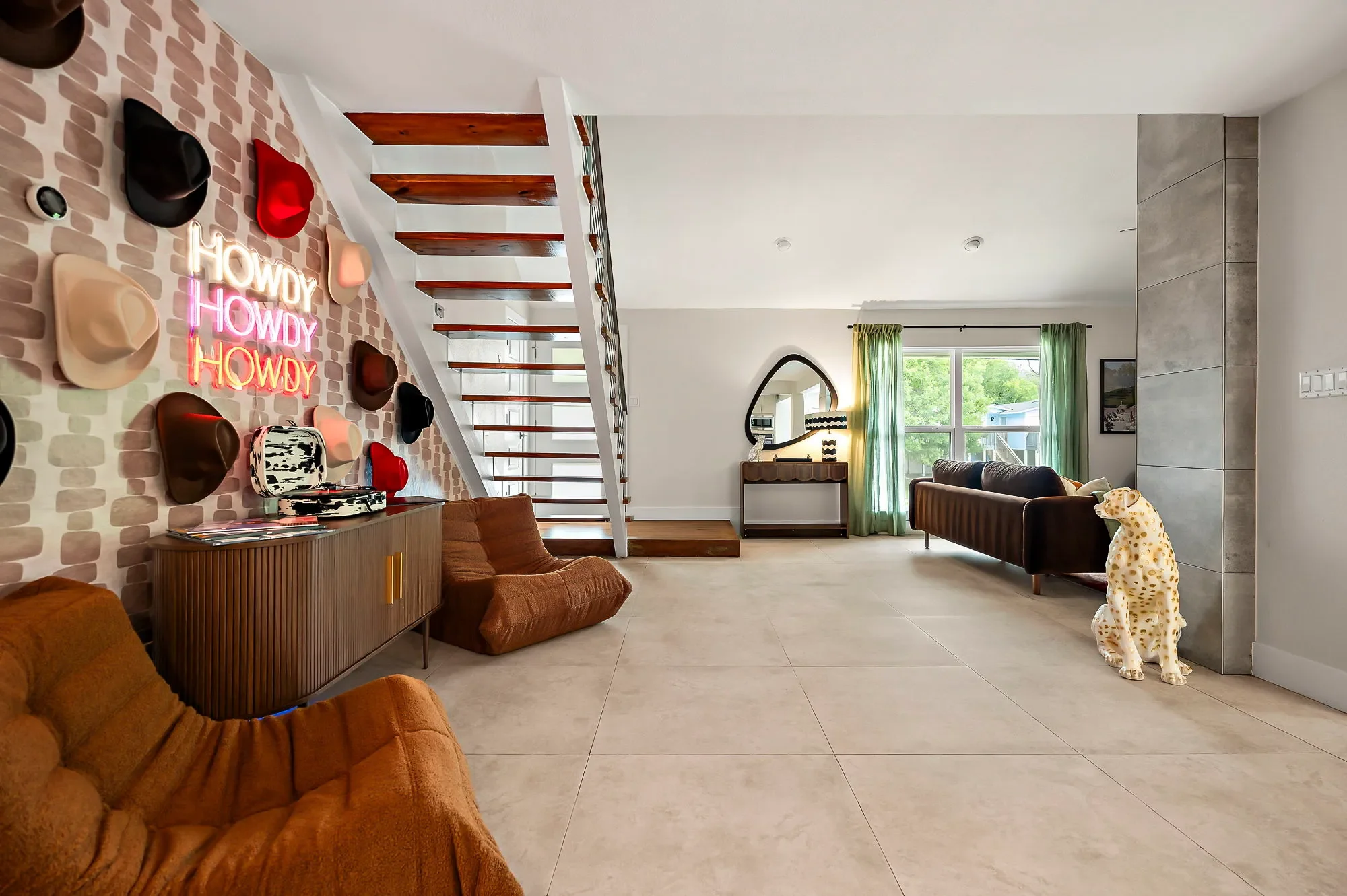 Short-term rental open plan design with cowboy hat wall, Howdy neon sign, togo chairs, floating staircase, and dalmatian statue — Austin TX.