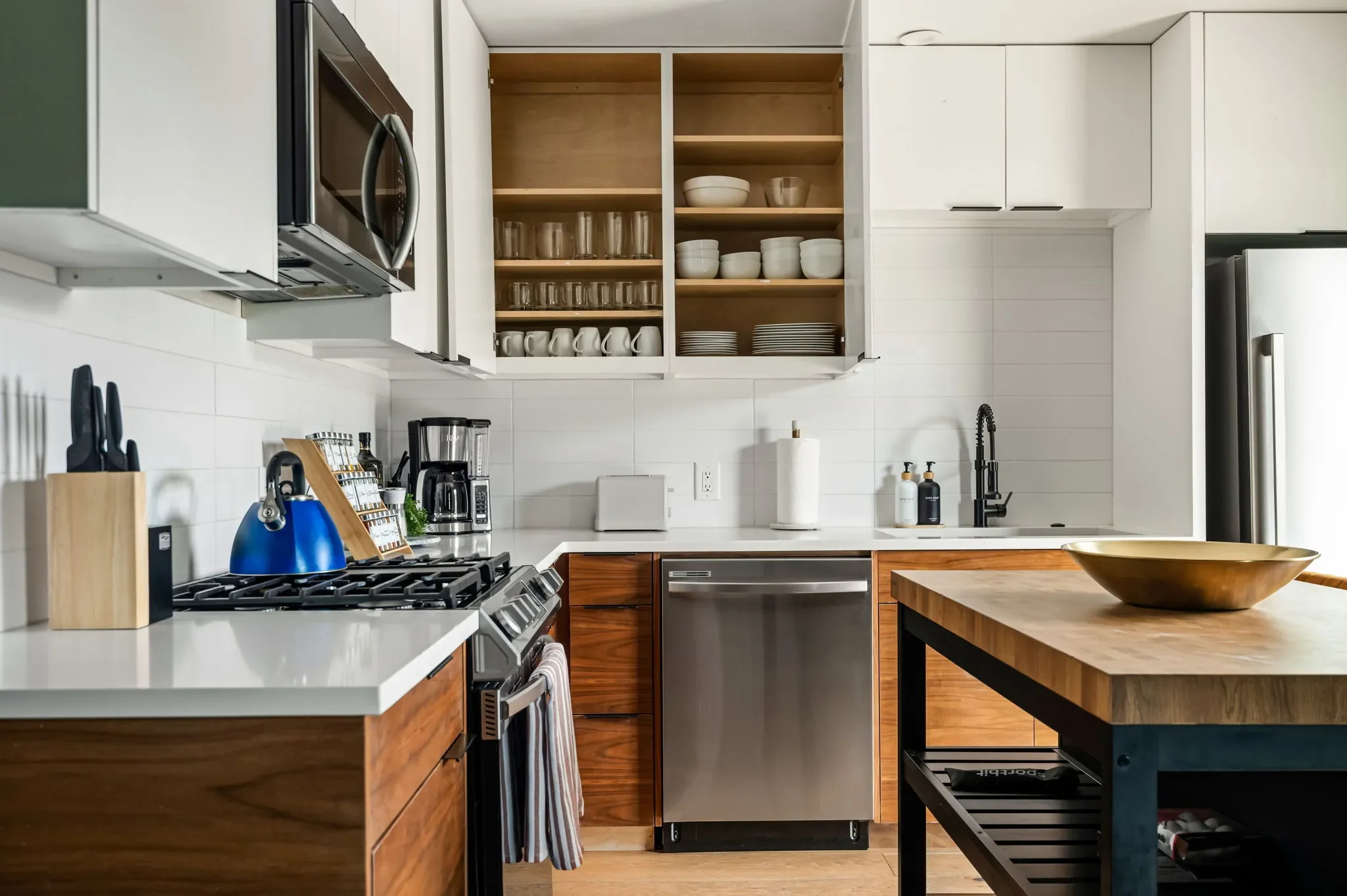 Airbnb guest house kitchen detail with open shelving, stainless appliances, wood lower cabinets, and fully stocked countertops — Austin TX.