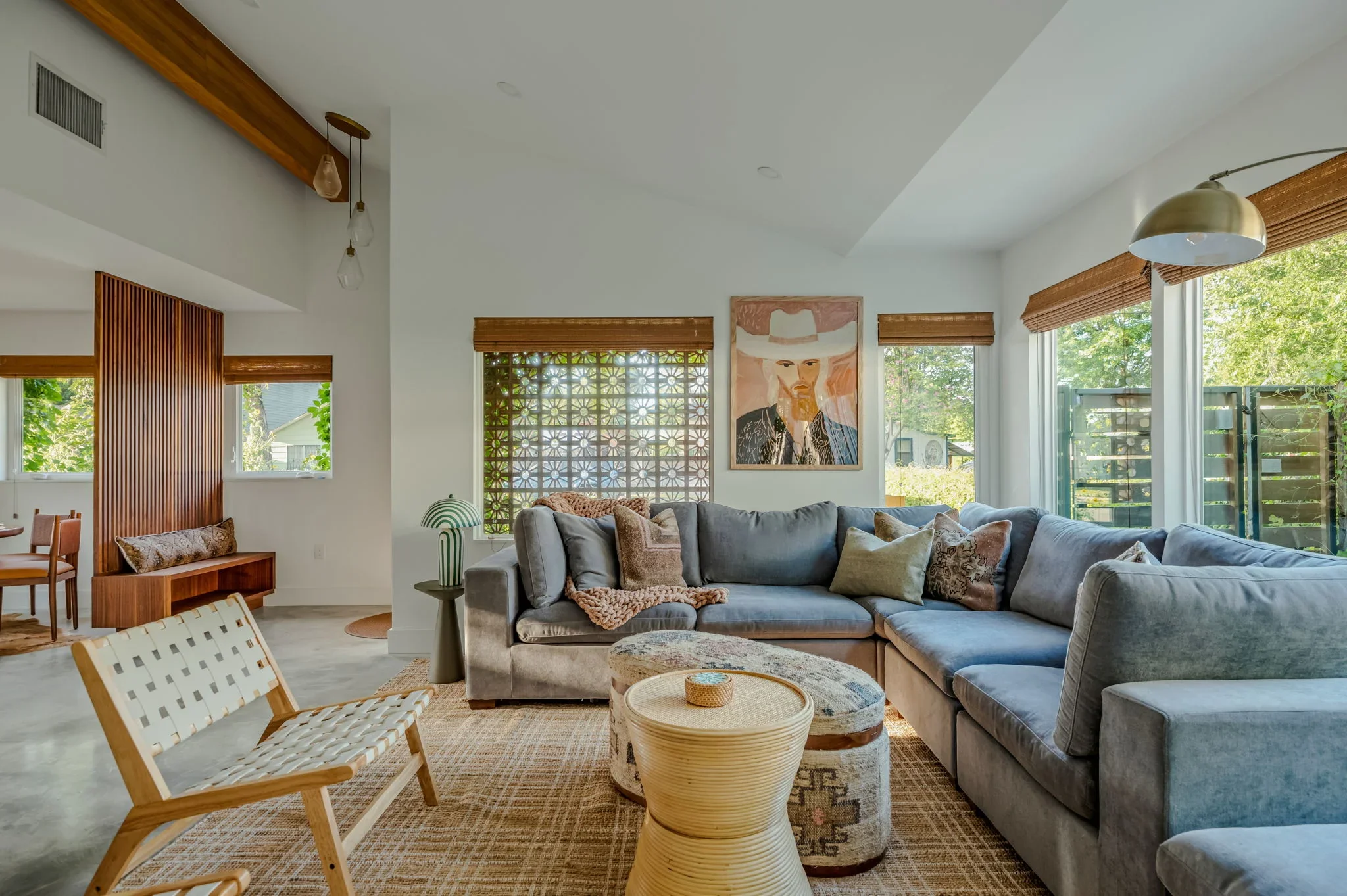 Short-term rental living room design with blue sectional, decorative breeze block wall, cowboy portrait art, and wood slat partition — Austin TX.
