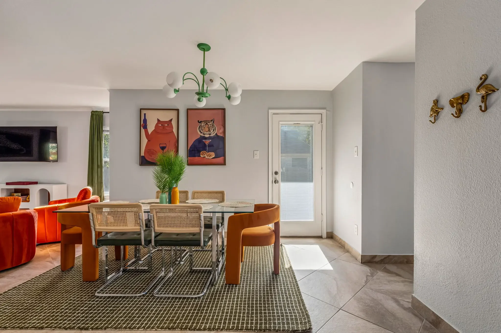 Short-term rental dining room design with eclectic animal wall art, orange chairs, green chandelier, and patterned rug — Austin TX.