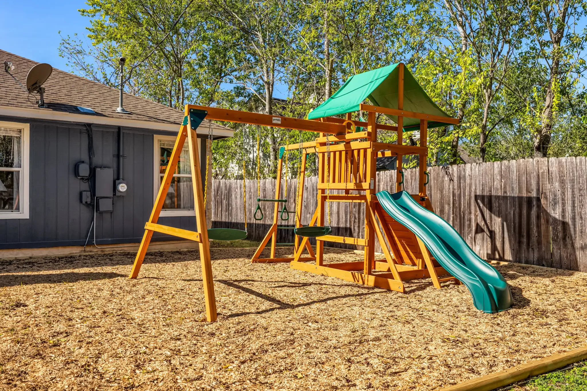 Outdoor area featuring a kids’ playground set with swings and a mulch play surface.