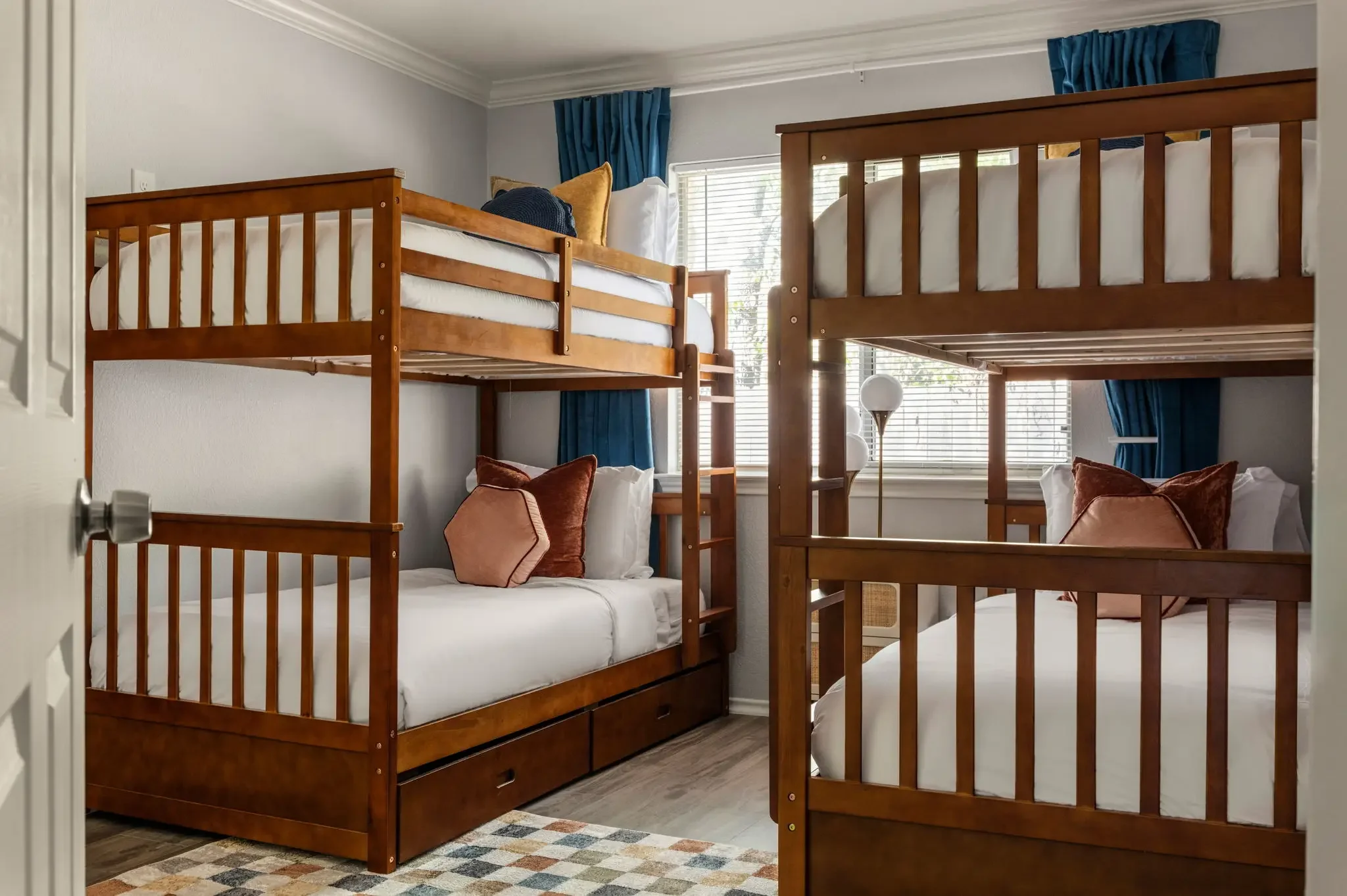 Airbnb bunk room design detail with wood bunk beds, colorful pillows, and navy curtains for family short-term rental — Austin TX.