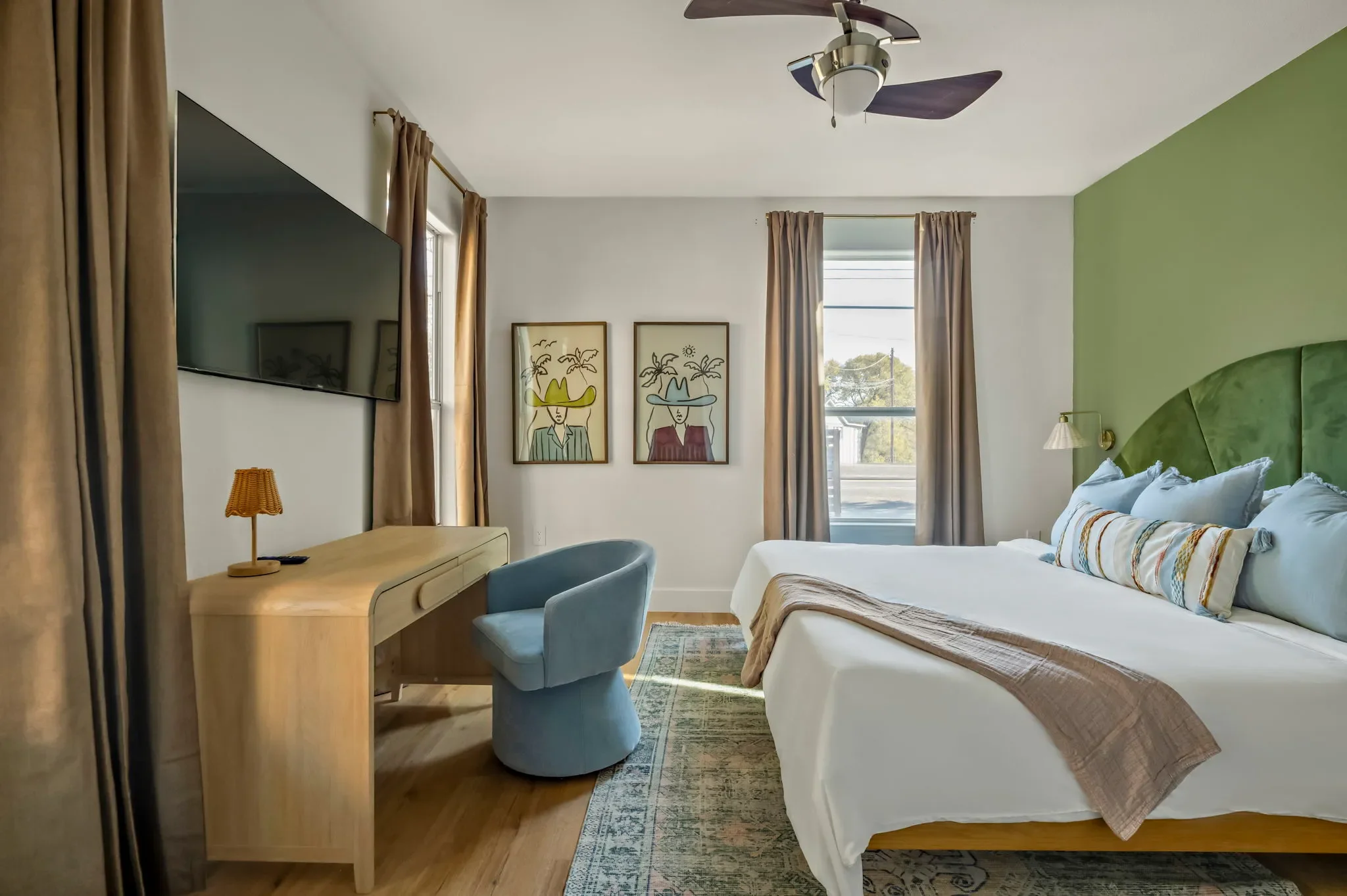 Short-term rental bedroom design with olive green accent wall, scalloped headboard, blue accent chair, and desk workspace — Austin TX.