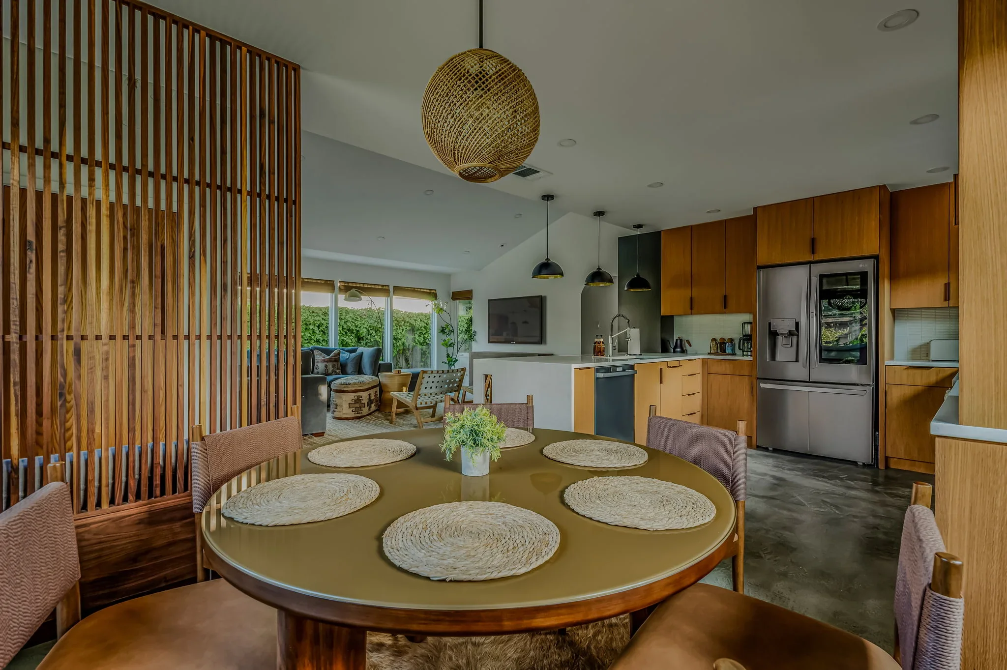 Short-term rental dining room design with round wood table, woven placemats, rattan pendant, and wood slat partition — Austin TX.