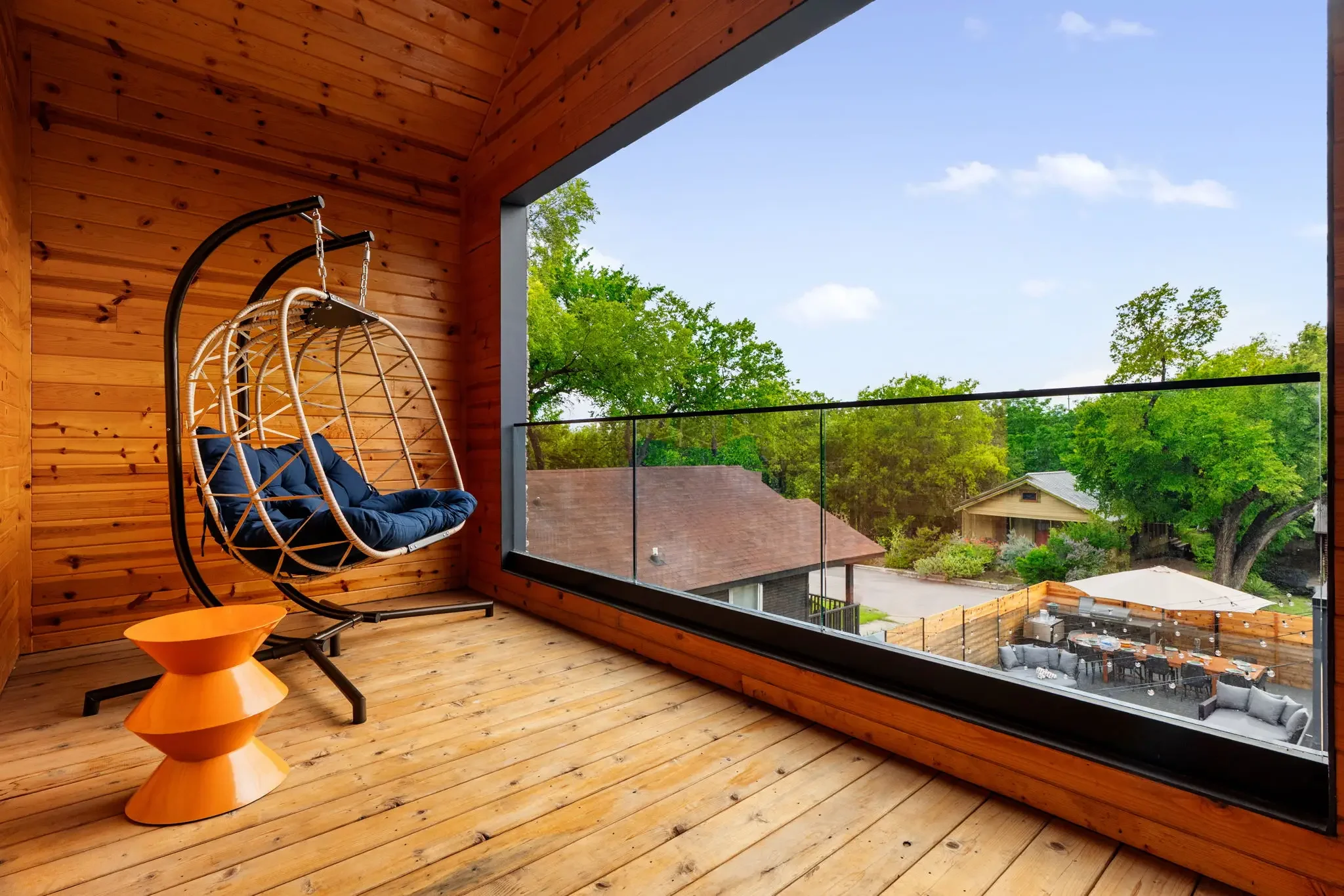 Airbnb outdoor design with hanging egg chairs, cedar wood ceiling, orange side table, and glass railing balcony view — Austin TX.