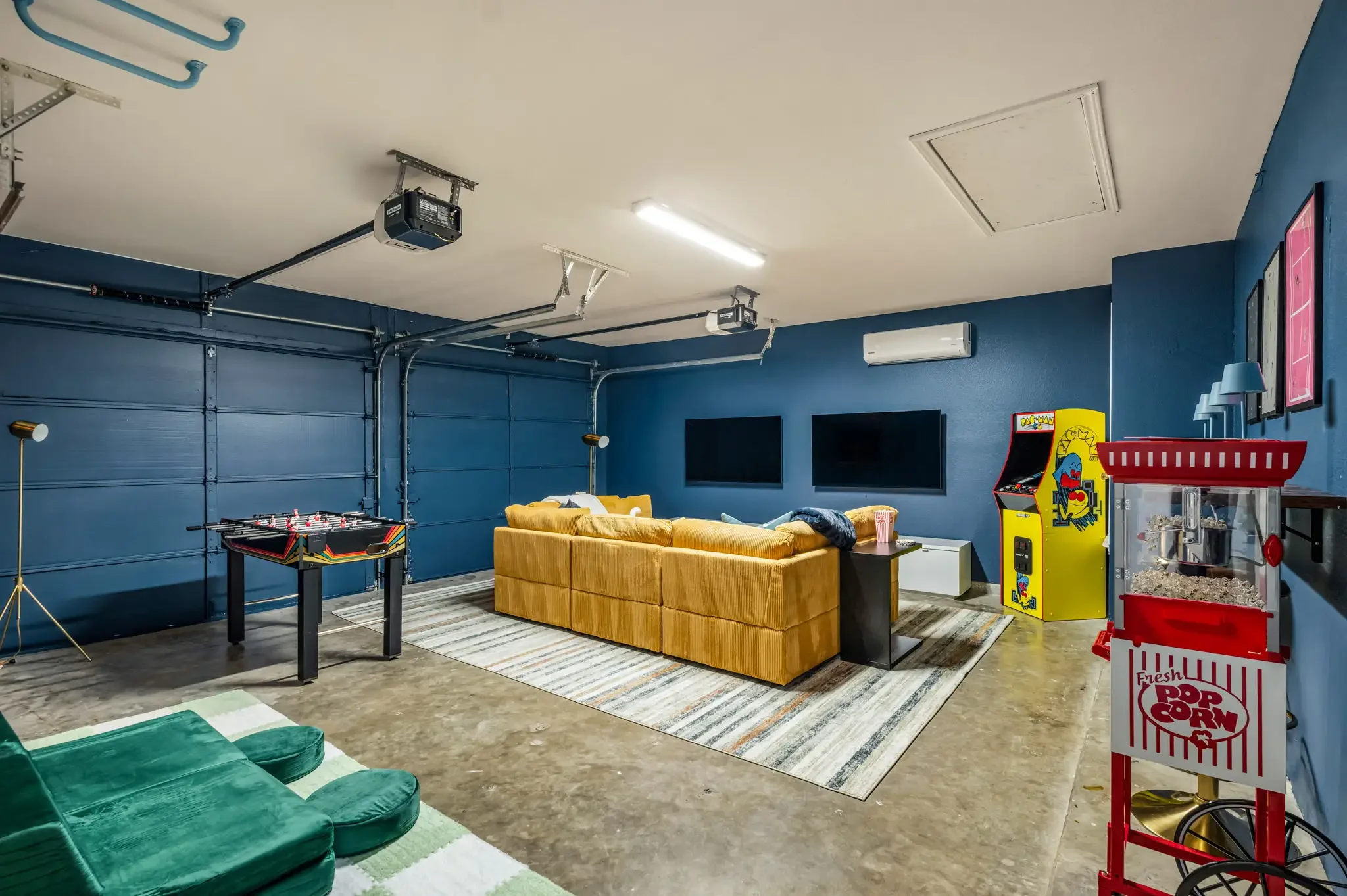 Short-term rental converted garage game room with foosball table, arcade machine, yellow sectional, and blue walls — Austin TX.