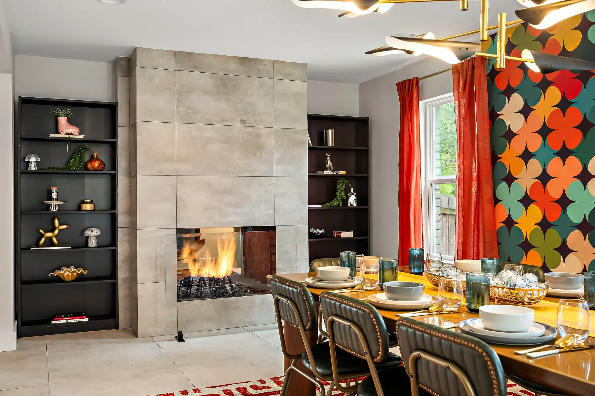 Airbnb dining room design with concrete fireplace, black built-in shelving, floral mural wall, and long set dining table — Austin TX.