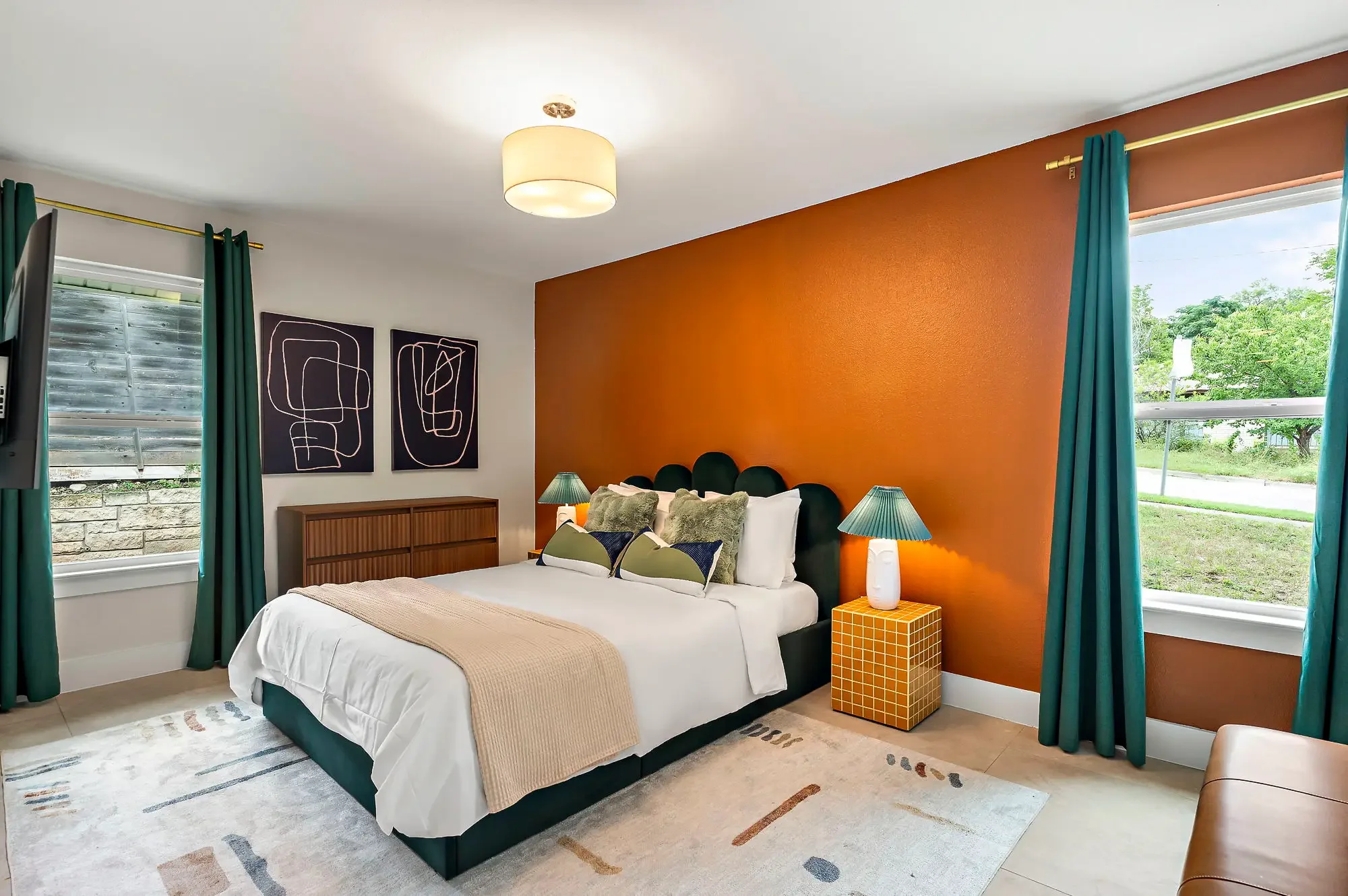 Short-term rental bedroom design with burnt orange accent wall, teal scallop headboard, teal curtains, and abstract wall art — Austin TX.