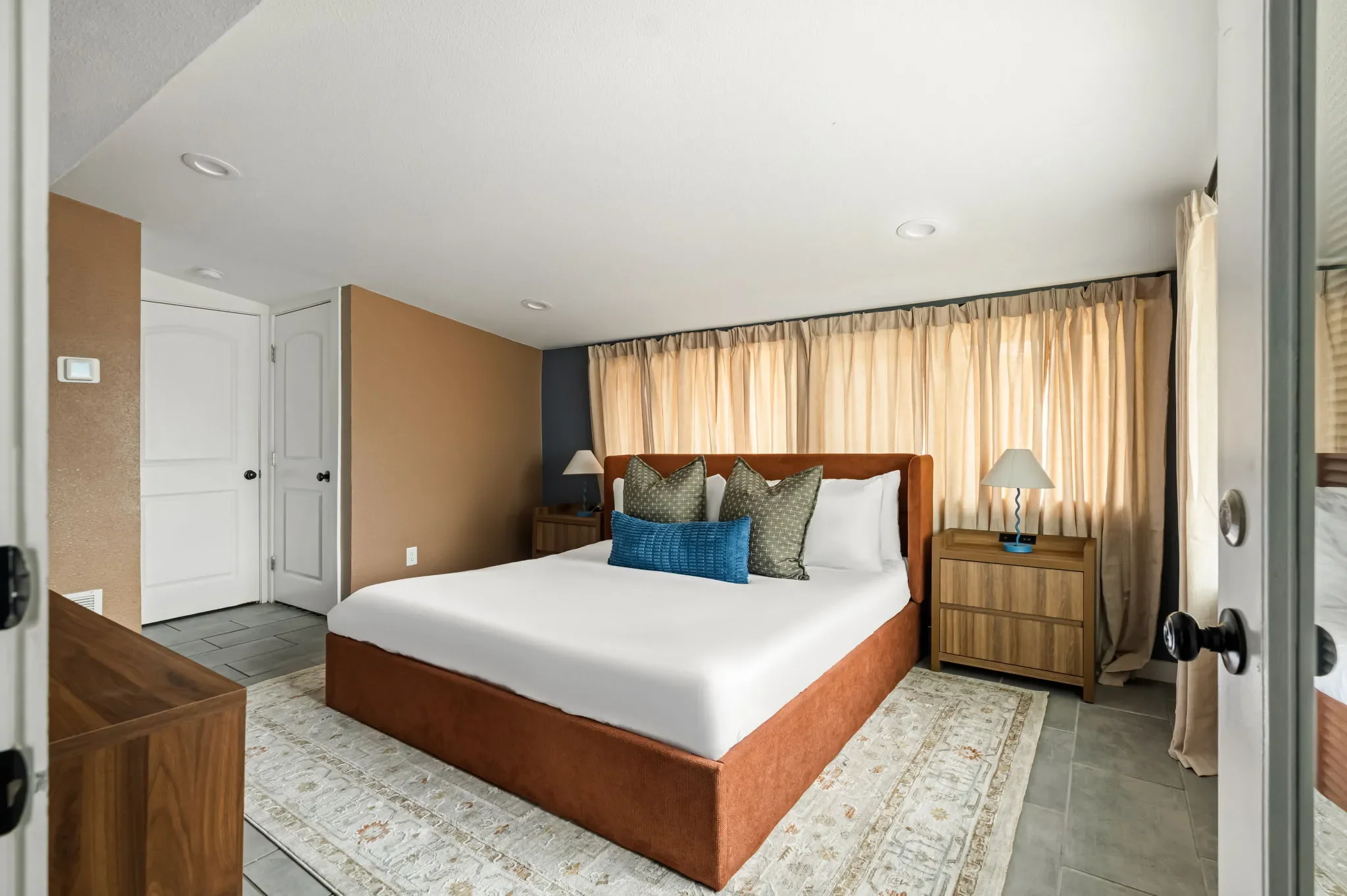 Short-term rental bedroom design with tan and blue walls, wood bed frame, linen curtains, and woven nightstand — Austin TX.