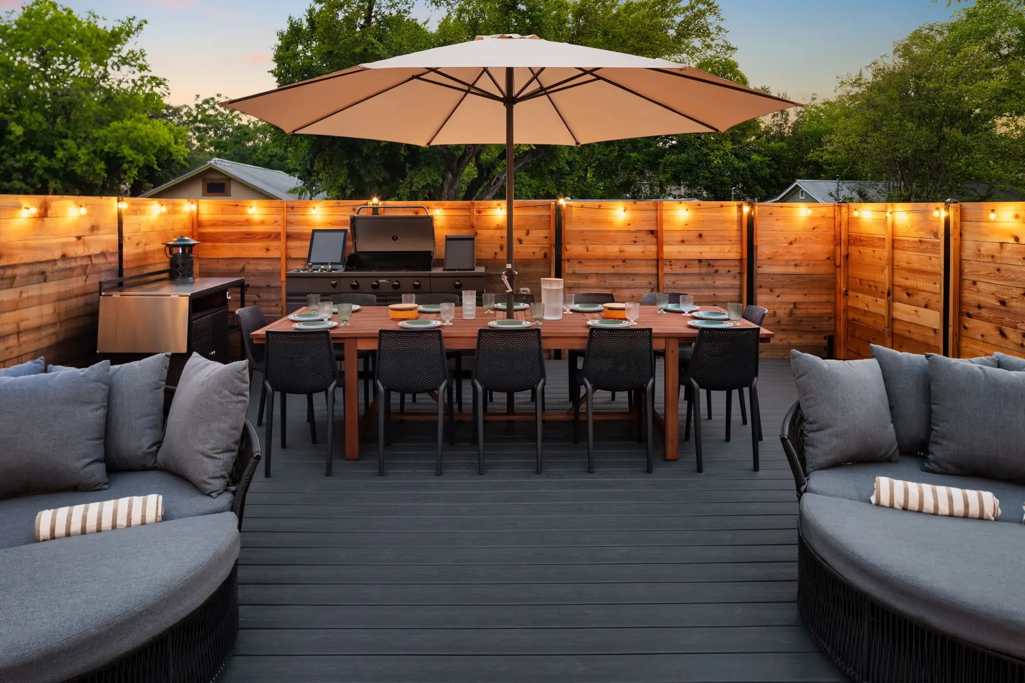 Outdoor patio with a large dining table and seating, string lights, full outdoor kitchen, and an umbrella.