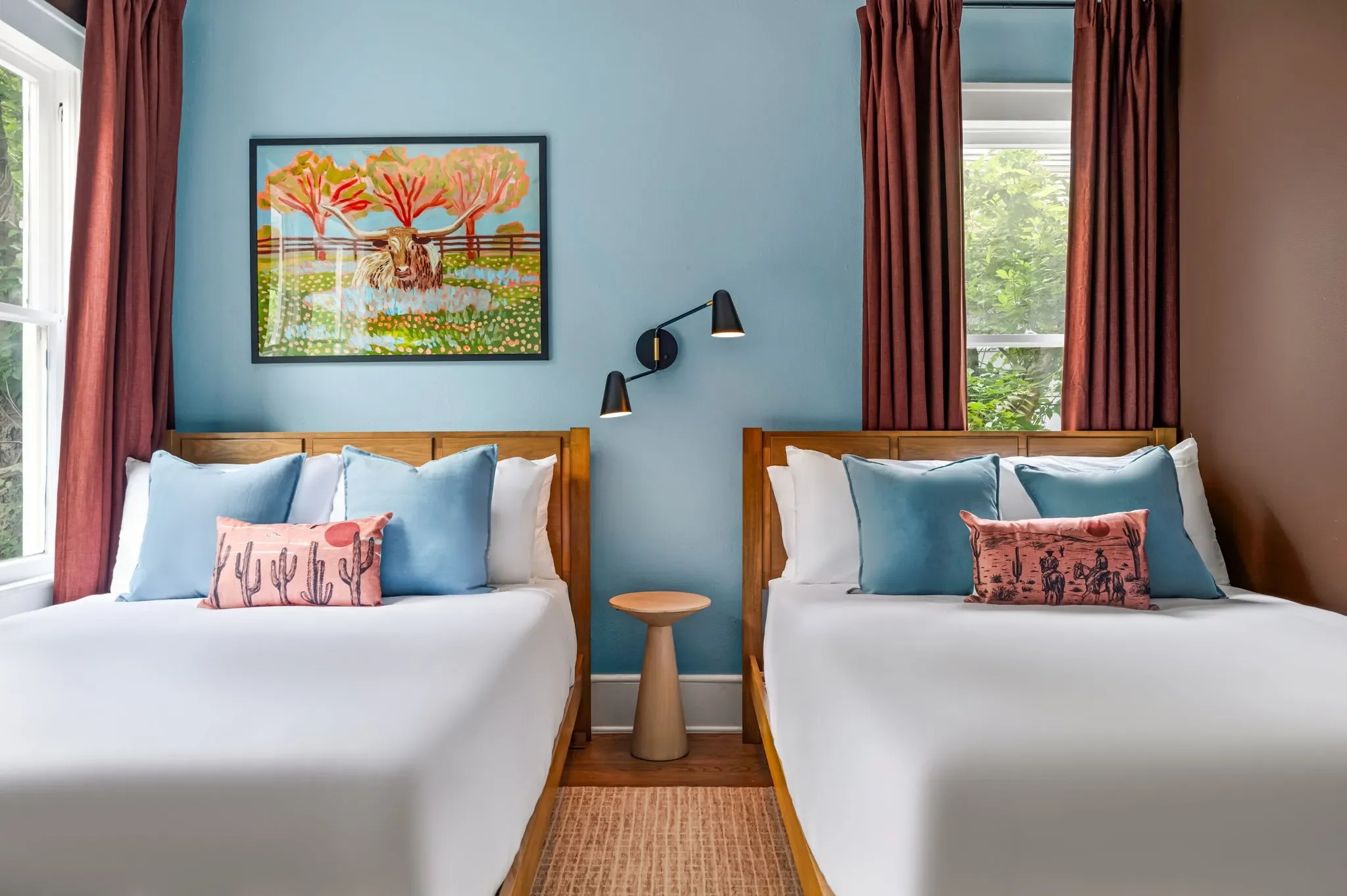 Short-term rental double bedroom design with blue accent wall, wood bed frames, blue and pink western pillows, and longhorn wall art — Austin TX.