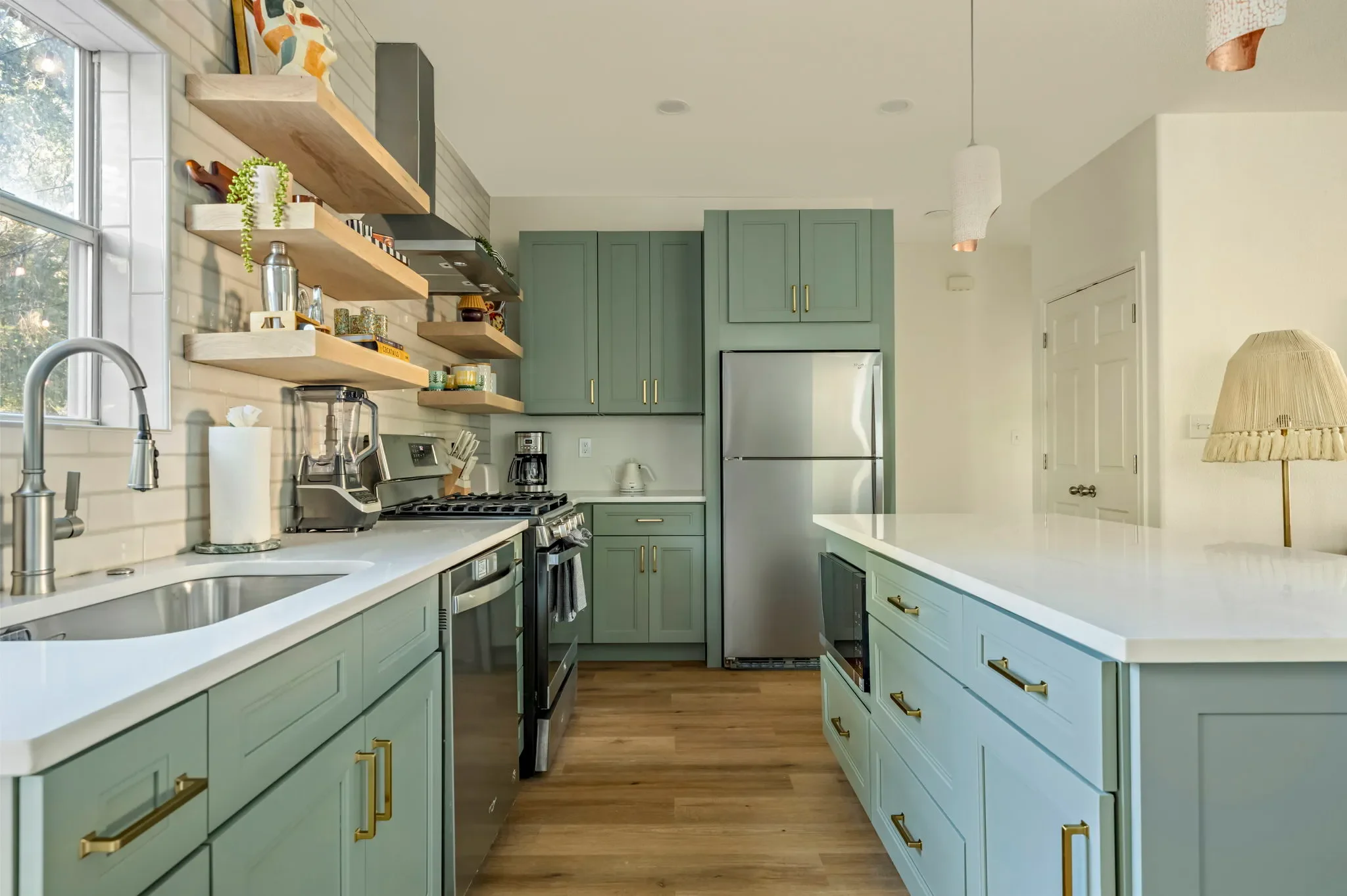 Airbnb kitchen design with sage green cabinets, white quartz counters, open wood shelving, and stainless appliances — Austin TX.