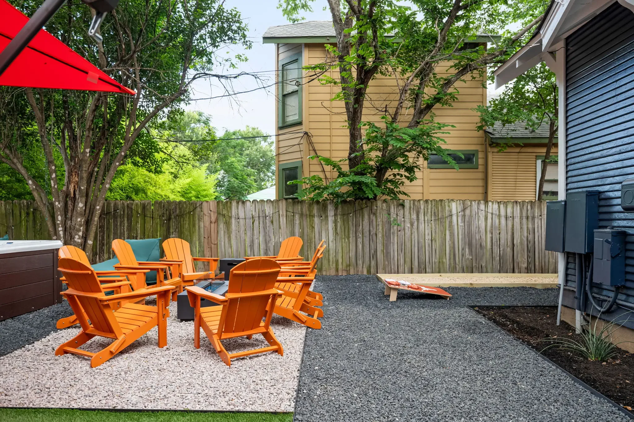 Short-term rental backyard design with fire pit, orange Adirondack chairs, cornhole boards, and gravel patio — Austin TX.