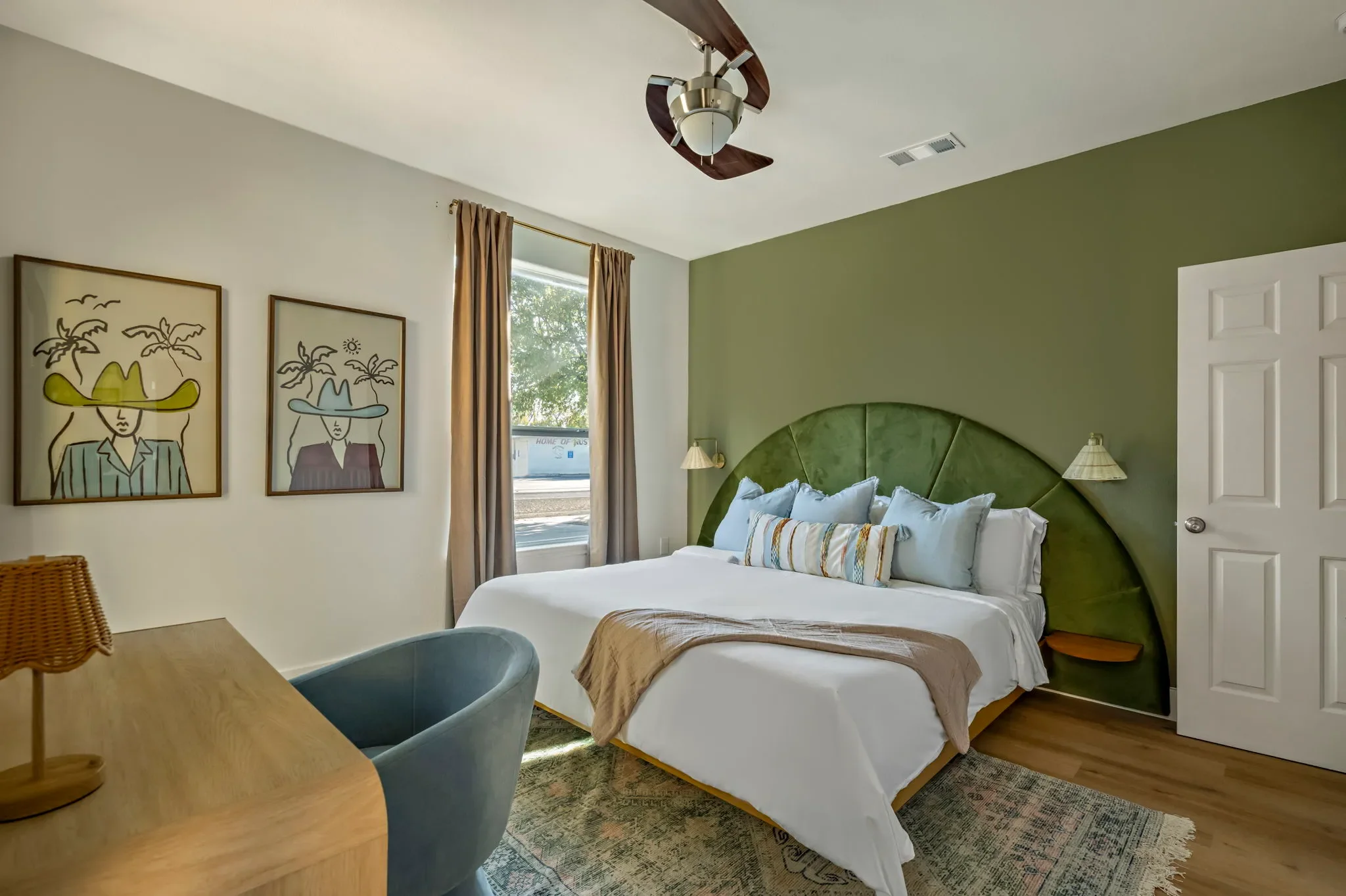 Bedroom with a green wall-mounted headboard, floating nightstands, cowboy wall art, a desk area, and a boho-style area rug.