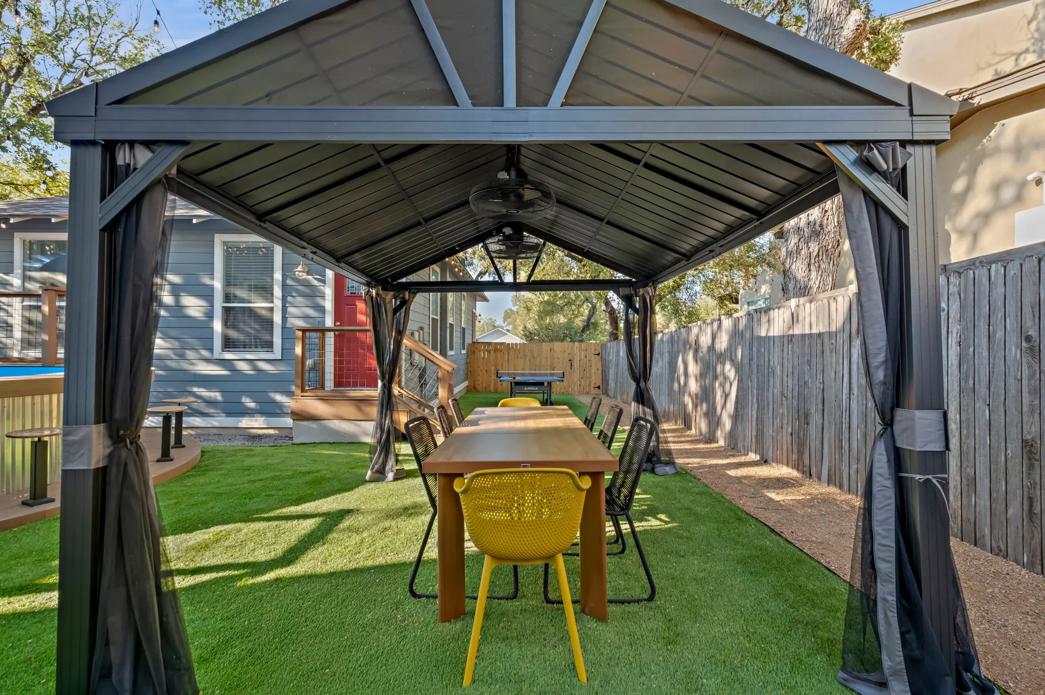 Airbnb outdoor design with screened gazebo, wood dining table, yellow chairs, and turf lawn — Austin TX.