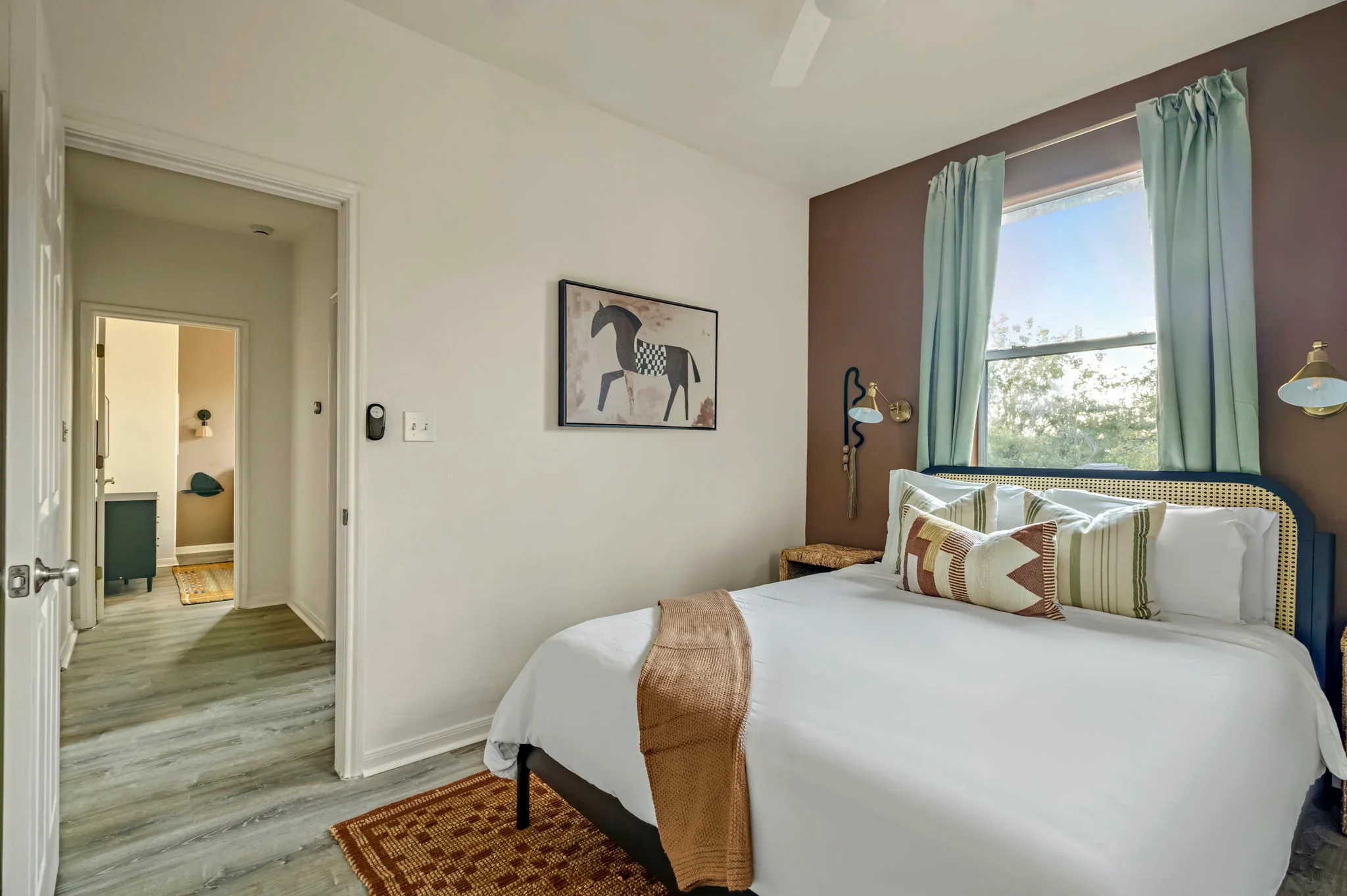 Short-term rental bedroom design with brown accent wall, sage curtains, cane headboard, and horse wall art — Austin TX.
