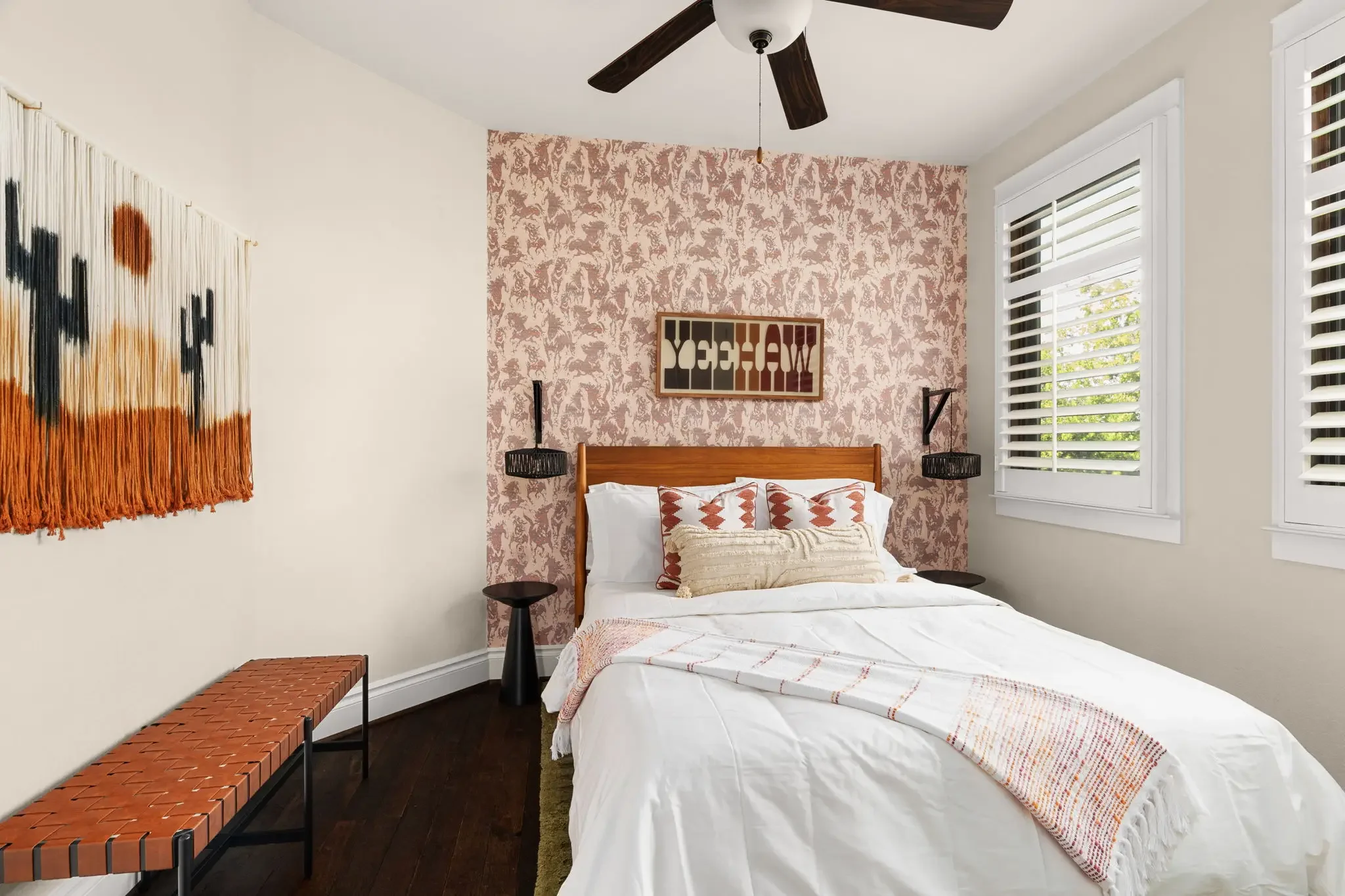Short-term rental bedroom with western horse wallpaper, wood headboard, woven bench, and Yeehaw wall art — Austin TX.