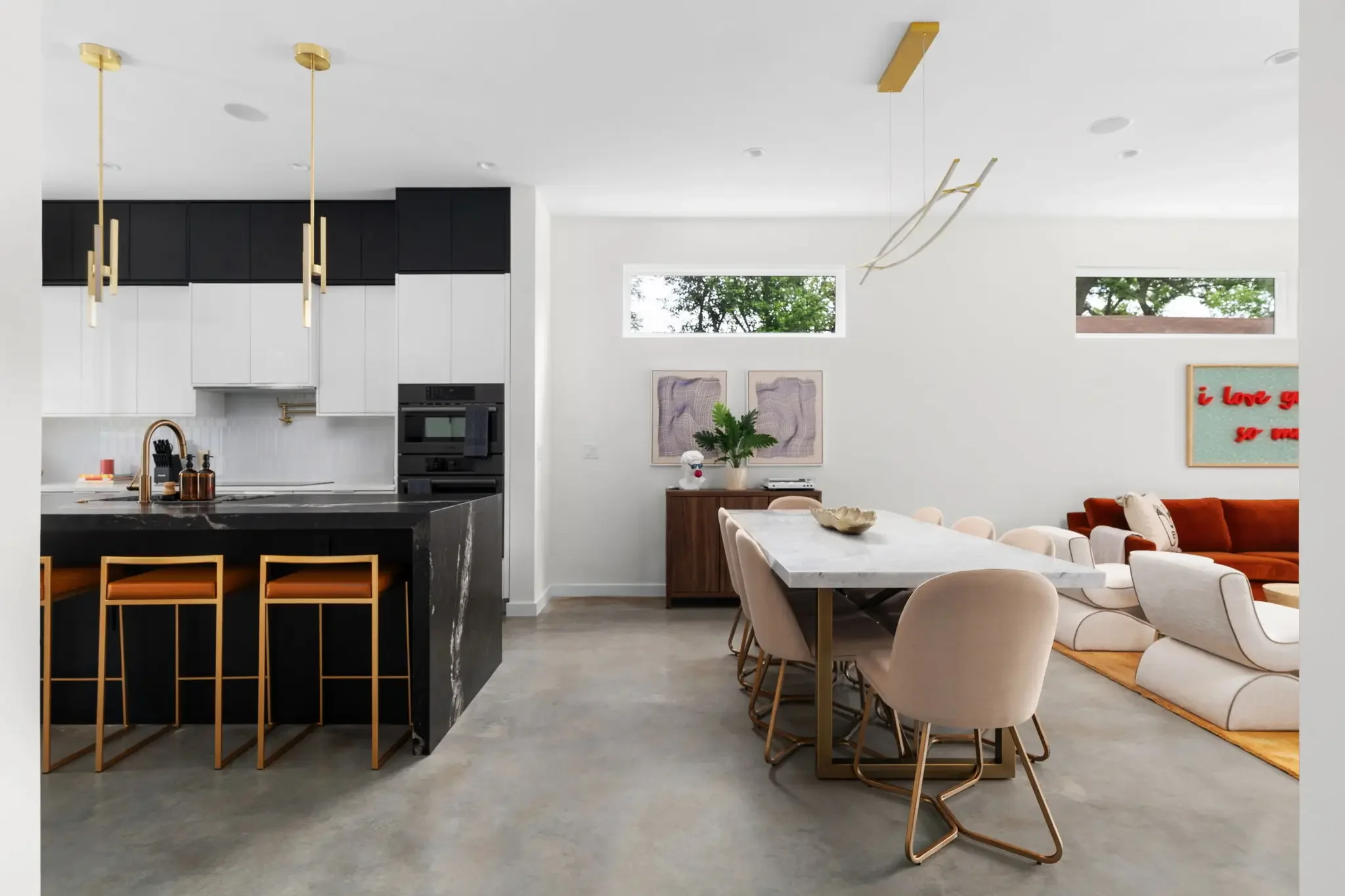 Short-term rental kitchen and dining design with black marble island, gold pendants, velvet dining chairs, and open plan living area — Austin TX.