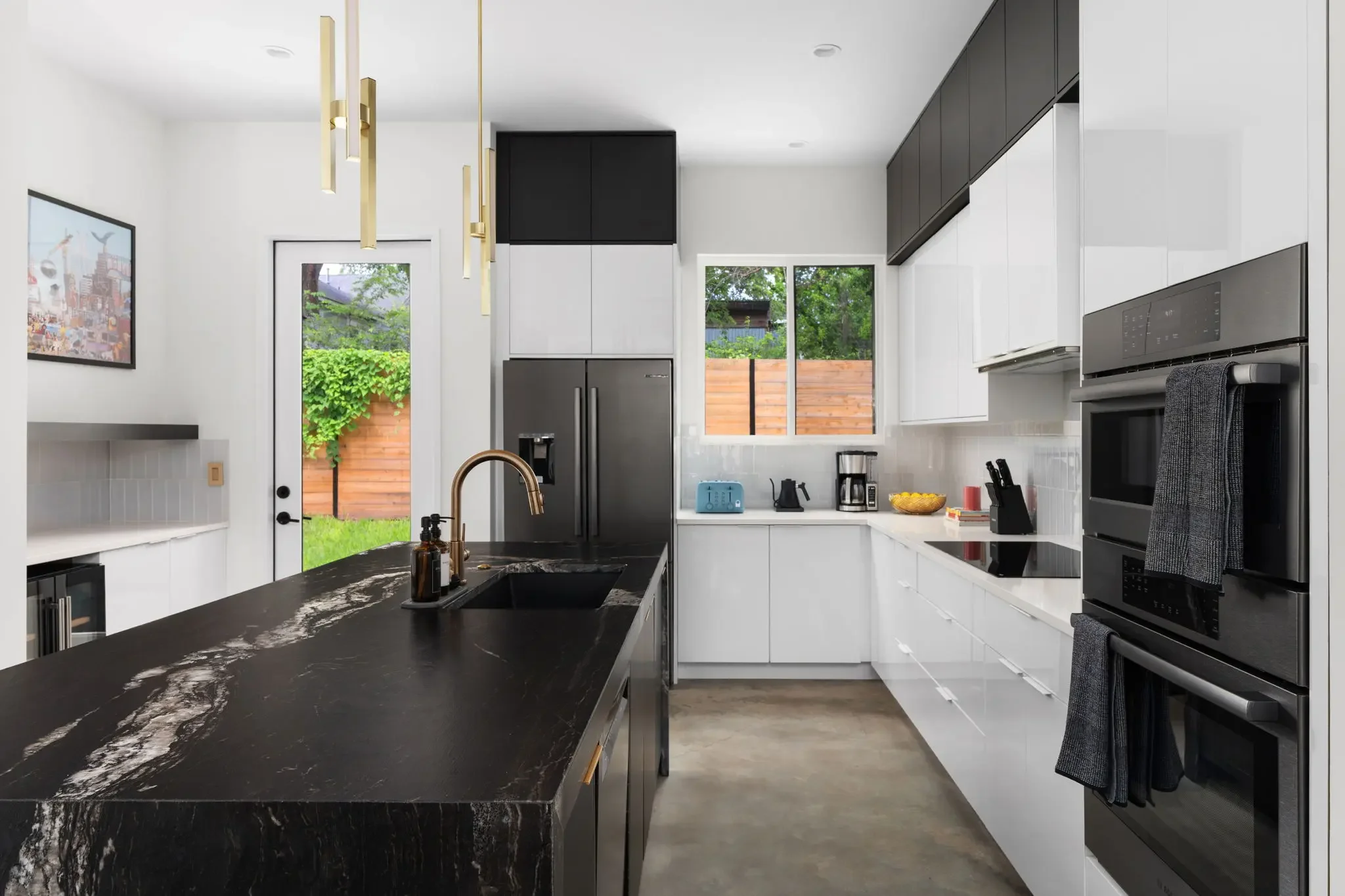 Contemporary modern kitchen with white cabinetry, black marble island, and gold accents.